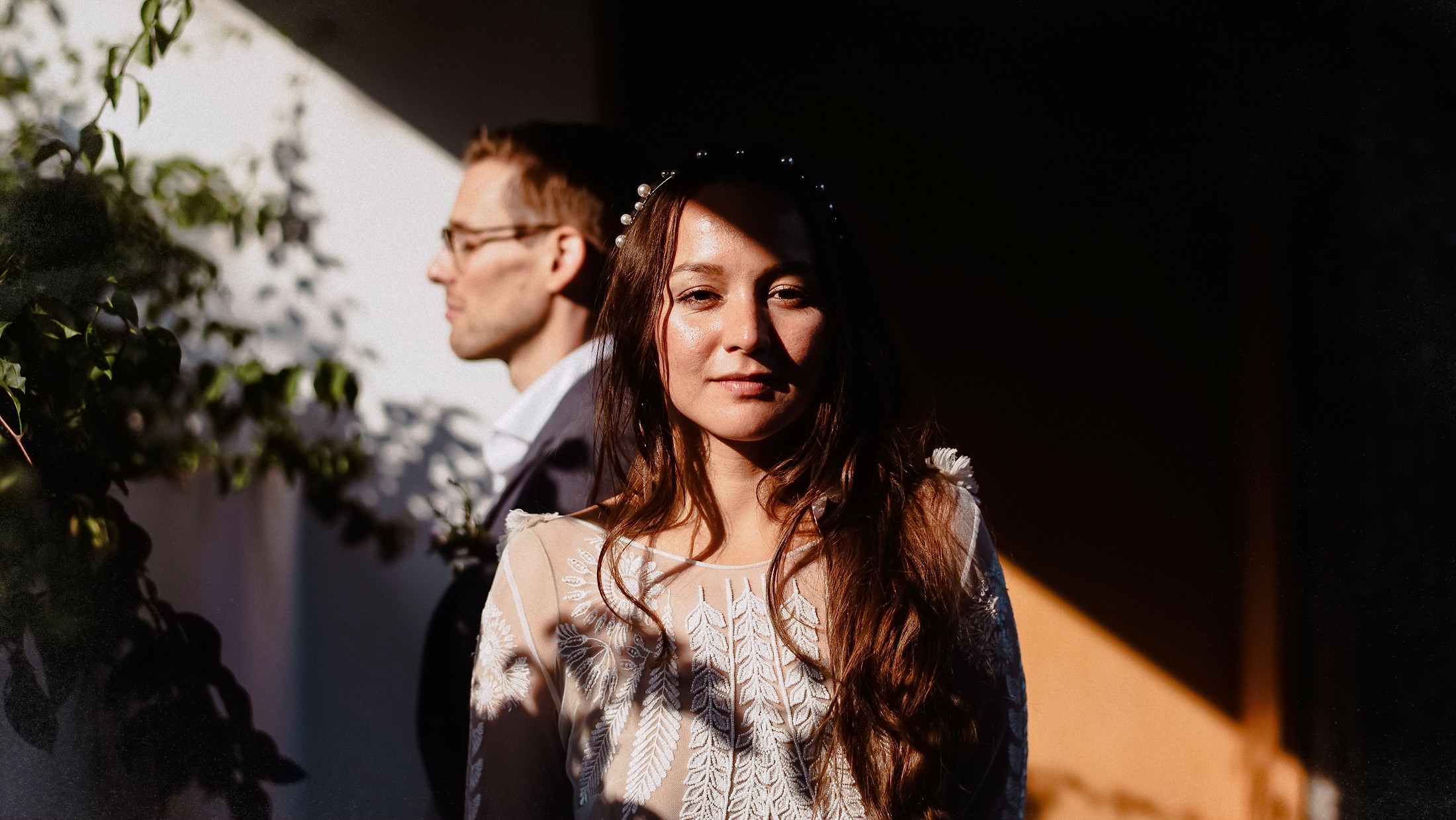 Portrait of Bride and Groom in a ray of light, the bride looking into the camera, groom has eyes closed