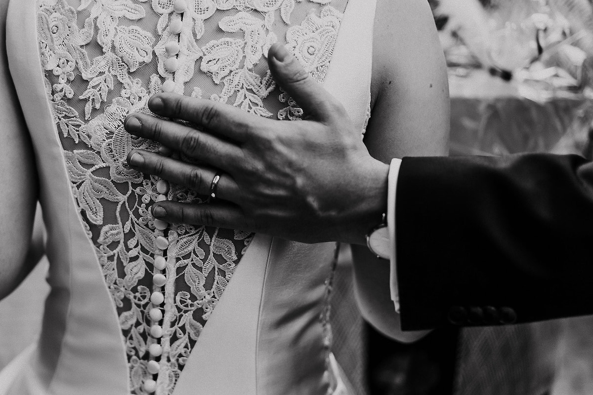 Bräutigam hält seine Hand an den Rücken seiner Braut, man sieht den Hochzeitsring