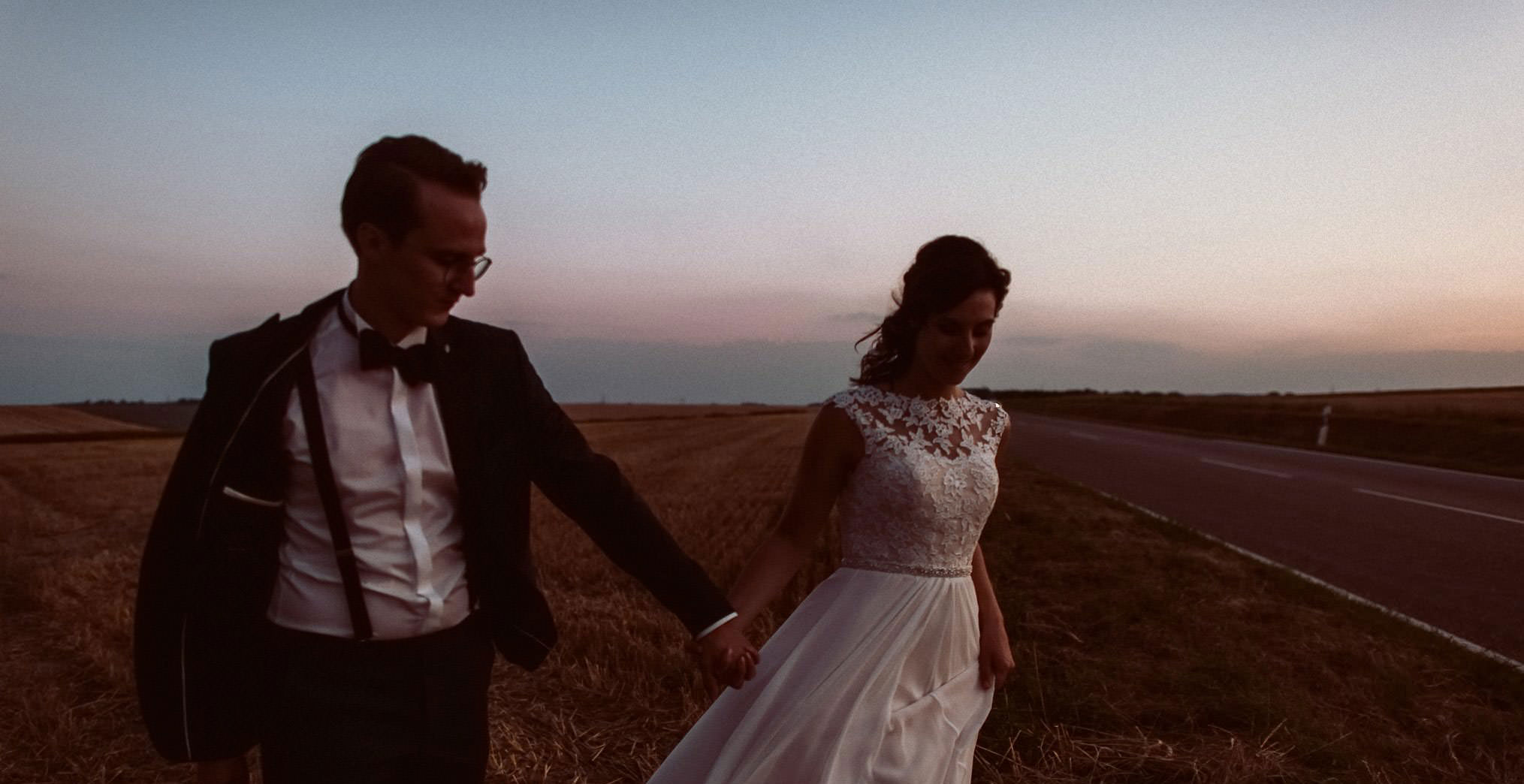 Ein Hochzeitspaar läuft Hand im Hand im Sonnenuntergang auf einem Feld