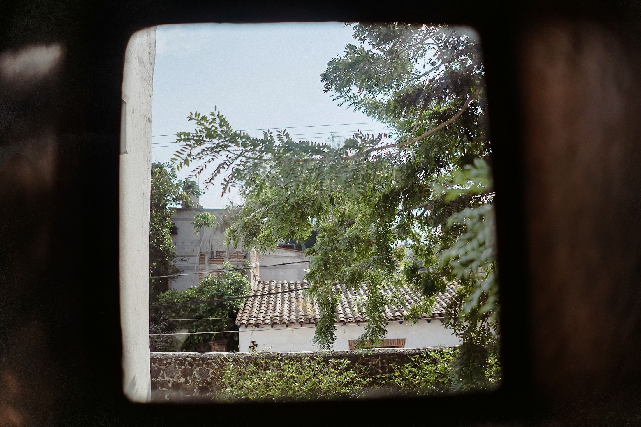 Der Blick durchs Fenster fällt auf einen mexikanischen Innenhof mit weißem Gebäude und Ziegeldach