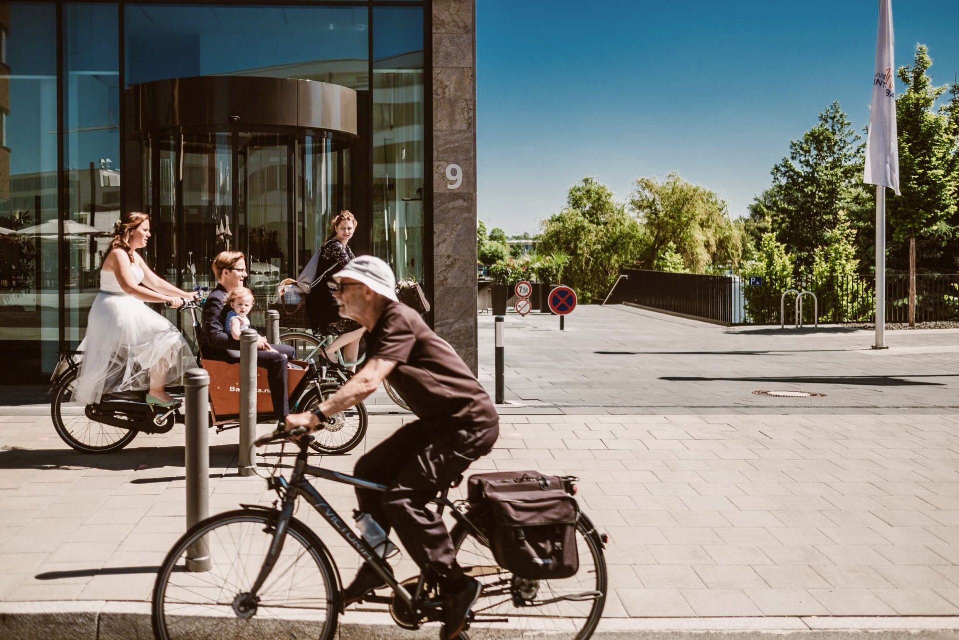 Das Brautpaar sitzt auf einem beladenen Lastenfahrrad in der sonnigen Innenstadt.