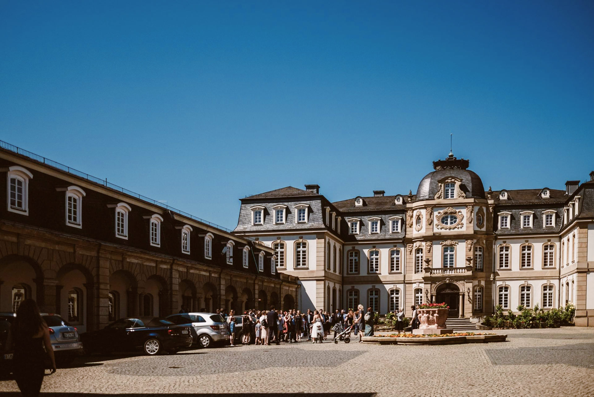 Das barocke Stadtpalais zeigt sich mit Hochzeitsgästen auf dem sonnigen Platz.