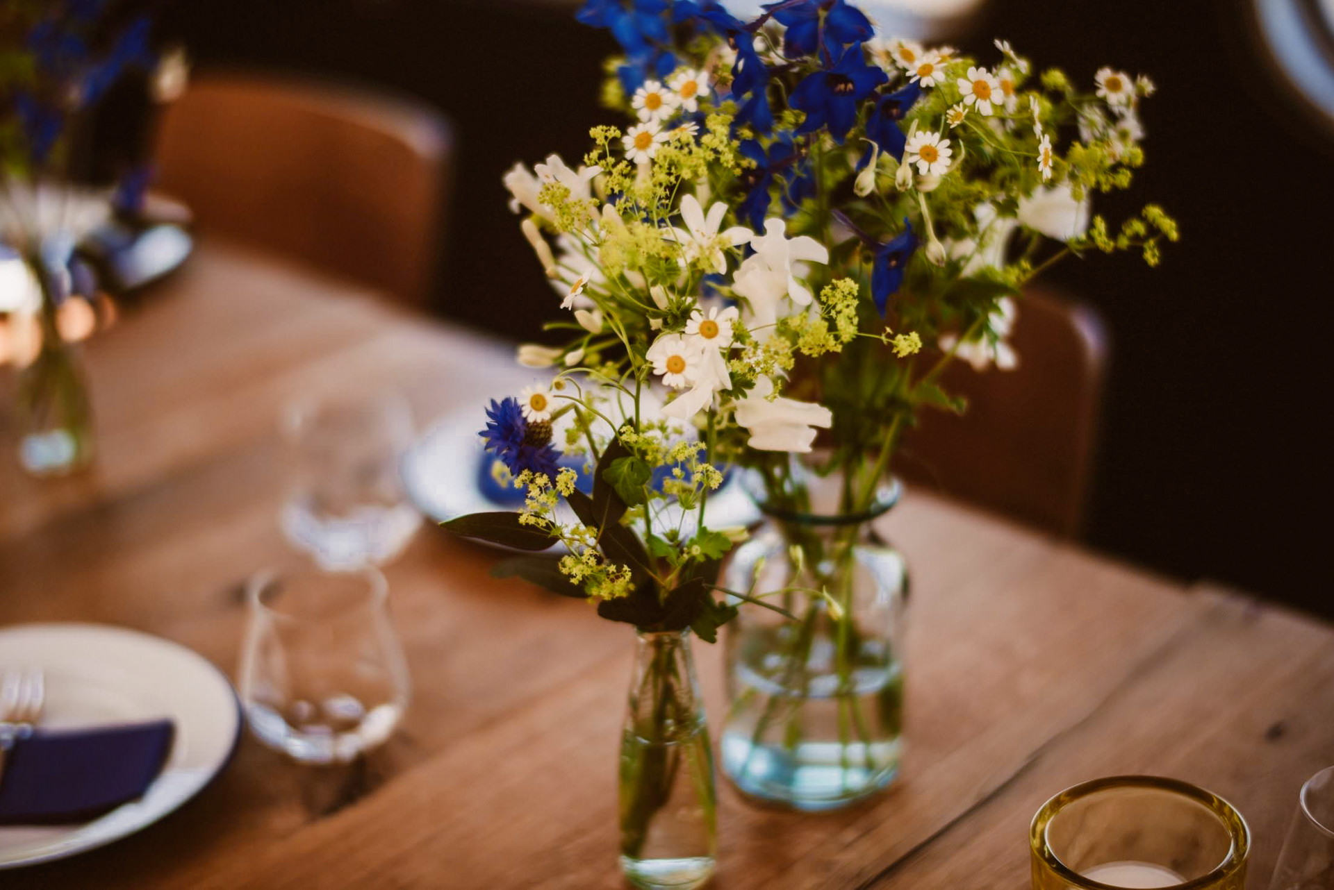 Das Tischgedeck zeigt Blumen mit blauen und gelben Blüten in Vasen.