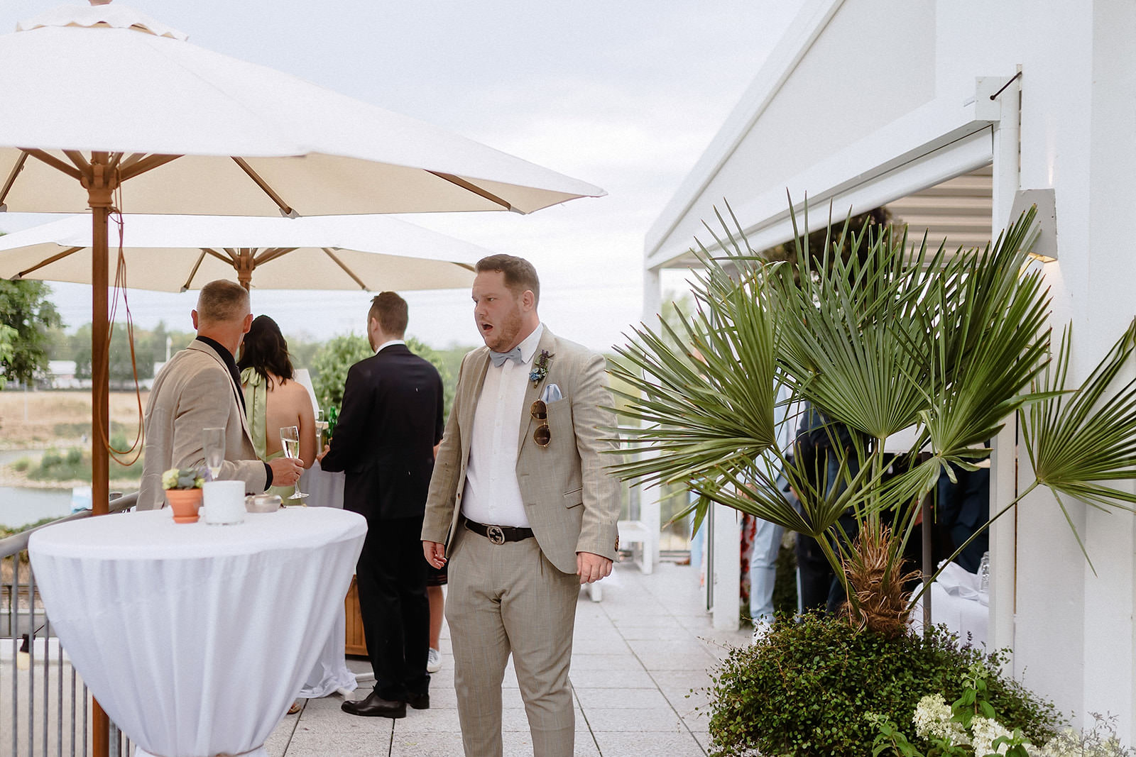 Ein Gast im beigen Anzug auf der Terrasse zwischen Sonnenschirmen und Palmen