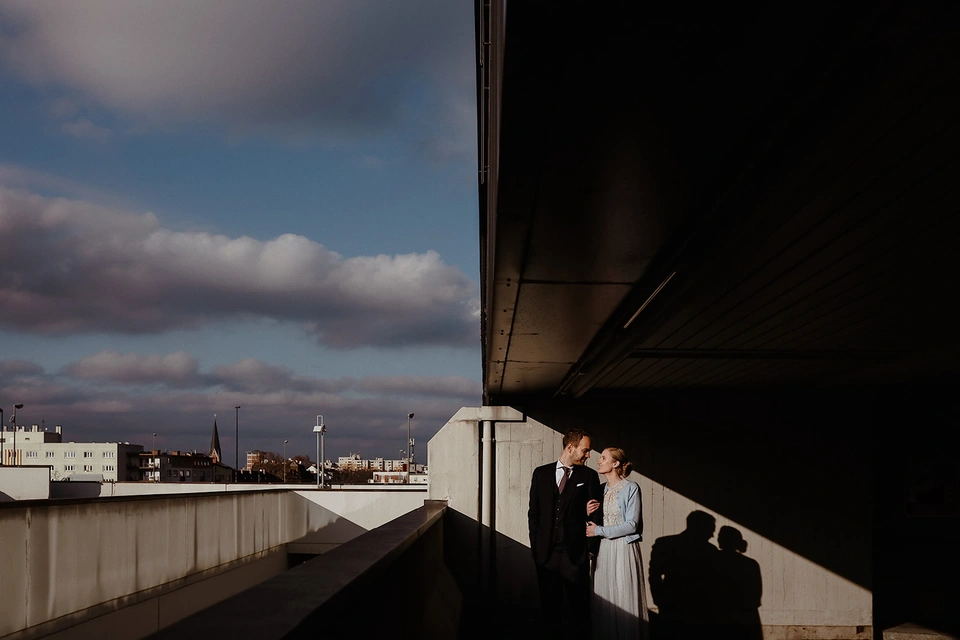 Brautpaar steht unter einem Gebäudeüberhang vor dramatischem Wolkenhimmel