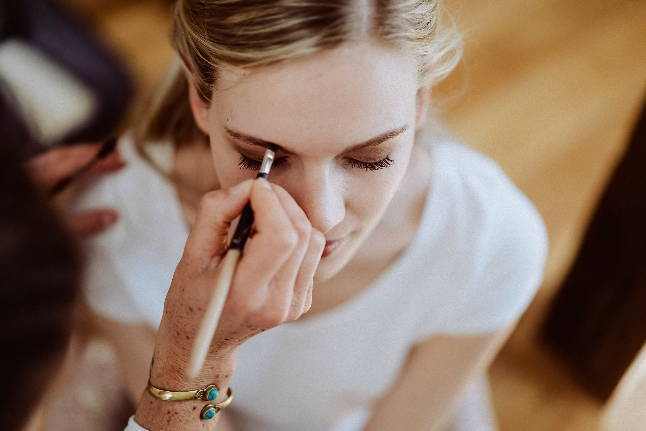 Der Braut werden mit einem Pinsel die Augenbrauen nachgezeichnet, die Augen geschlossen.