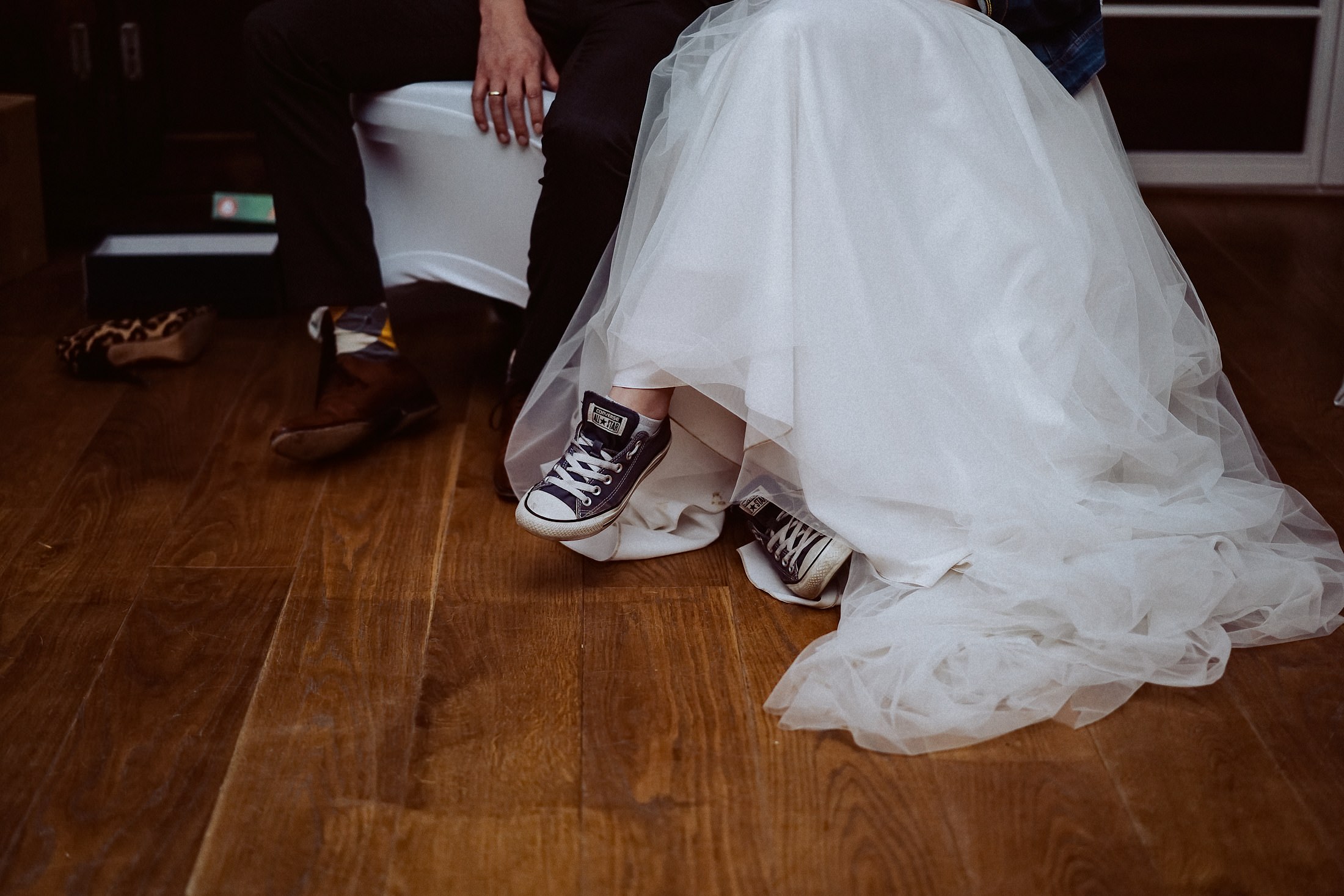 Unter dem Tüllrock der Braut kommen schwarze Sneaker hervor, daneben stehen Schuhkartons.