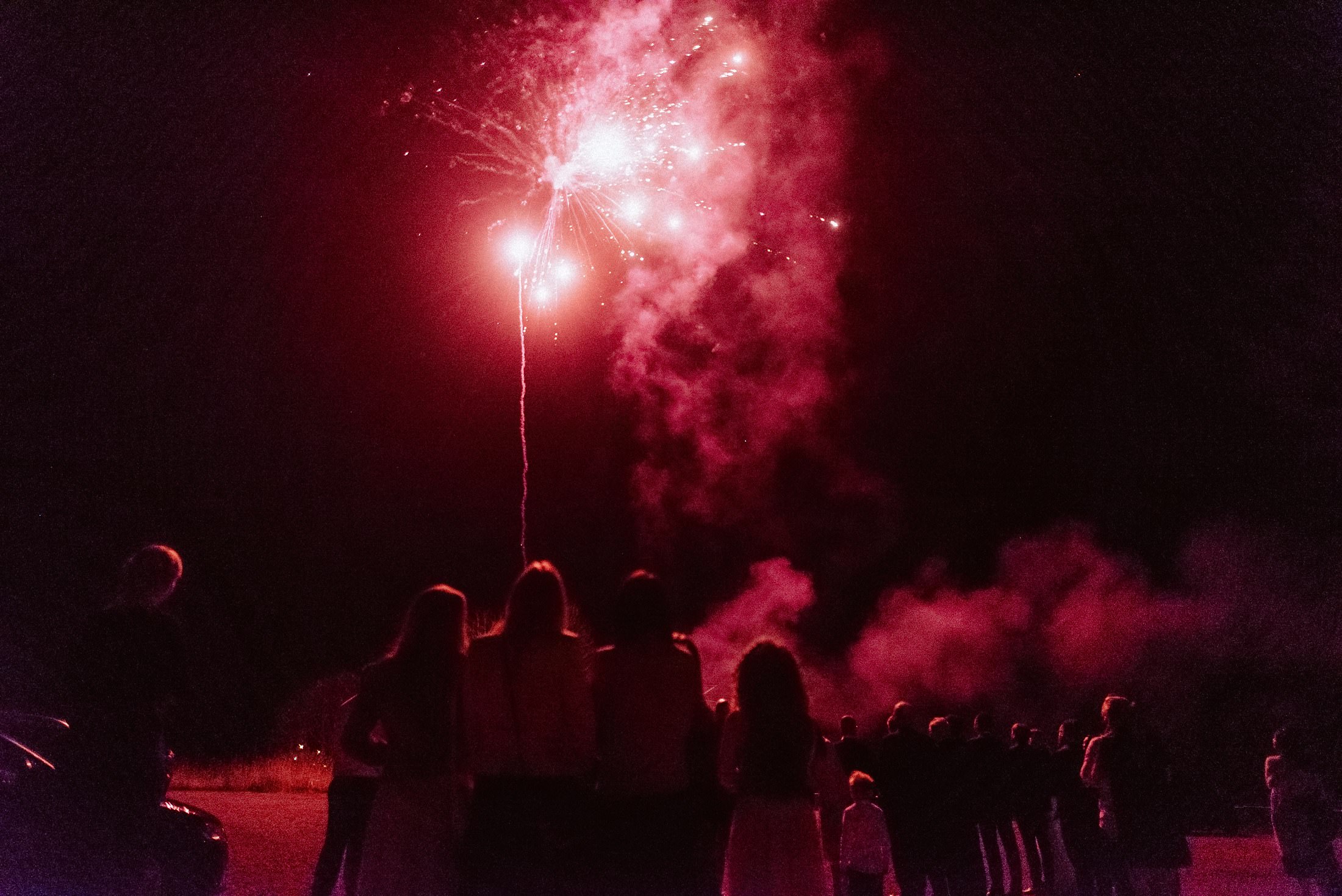 Rotes Feuerwerk leuchtet über dem Hof, Gäste schauen als Silhouetten zu.