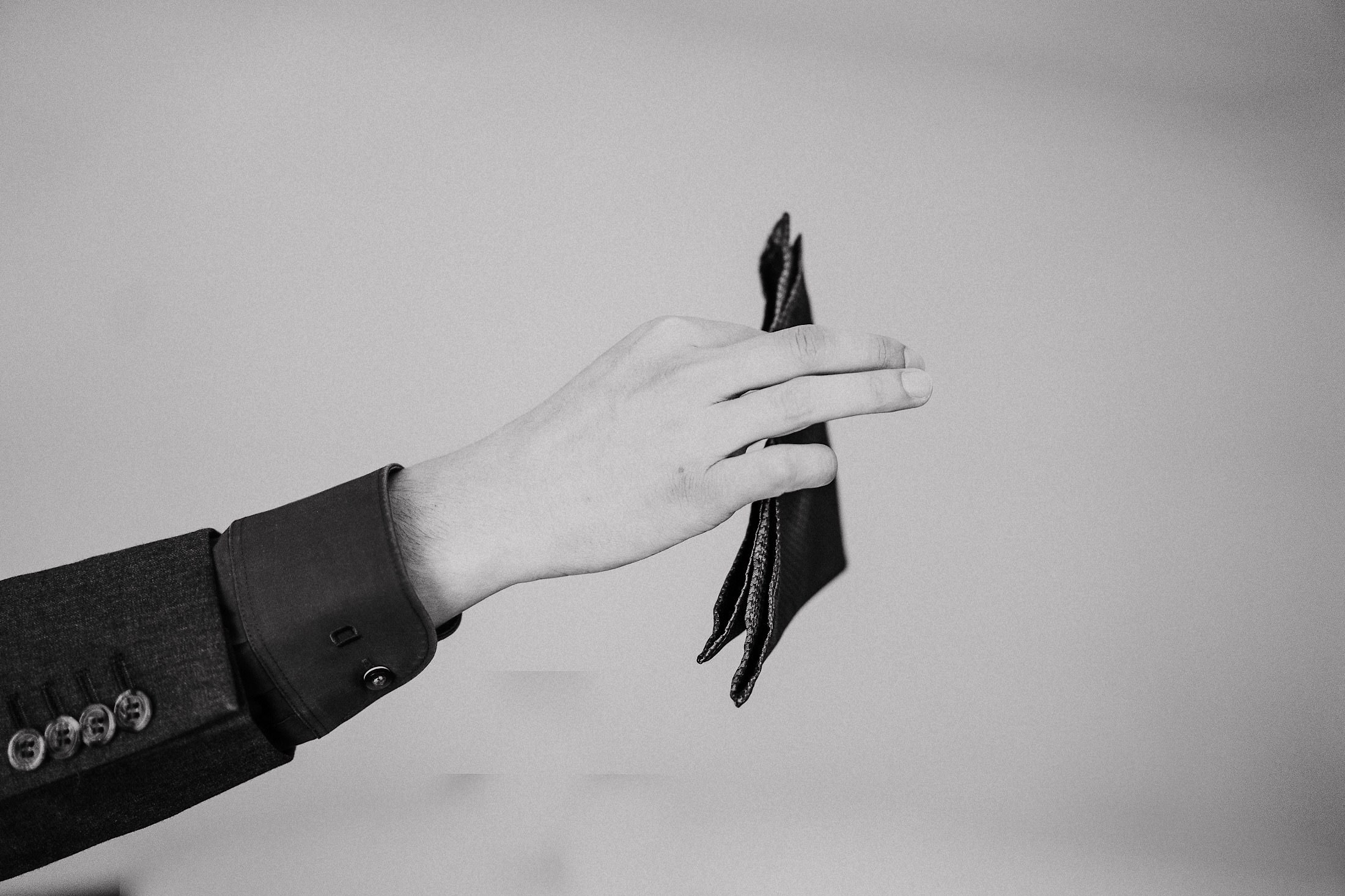 Eine Hand hält die noch ungebundene gestreifte Fliege vor hellem Hintergrund.