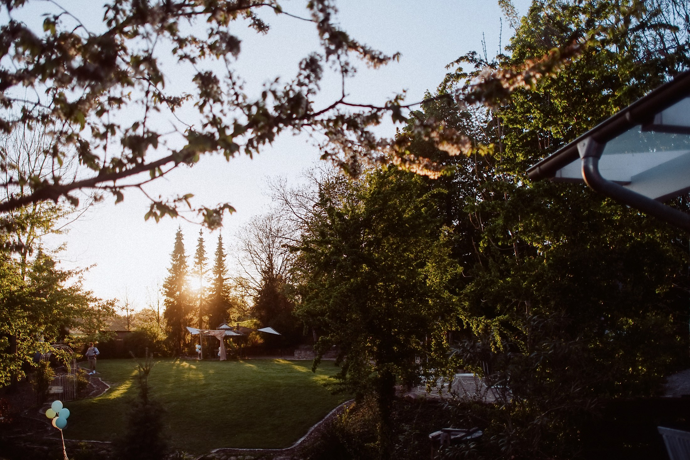 Die Abendsonne geht hinter den Bäumen im Garten der Eventmühle unter, davor bunte Luftballons.