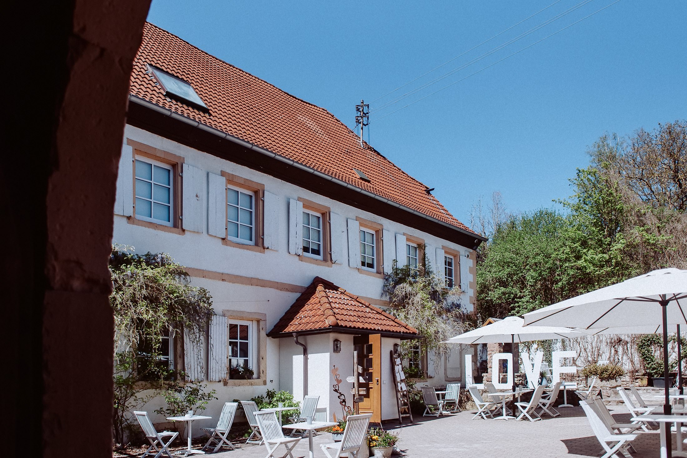 Der Innenhof des Dreiseithofs mit weißen Tischen, Sonnenschirmen und großen LOVE-Buchstaben.