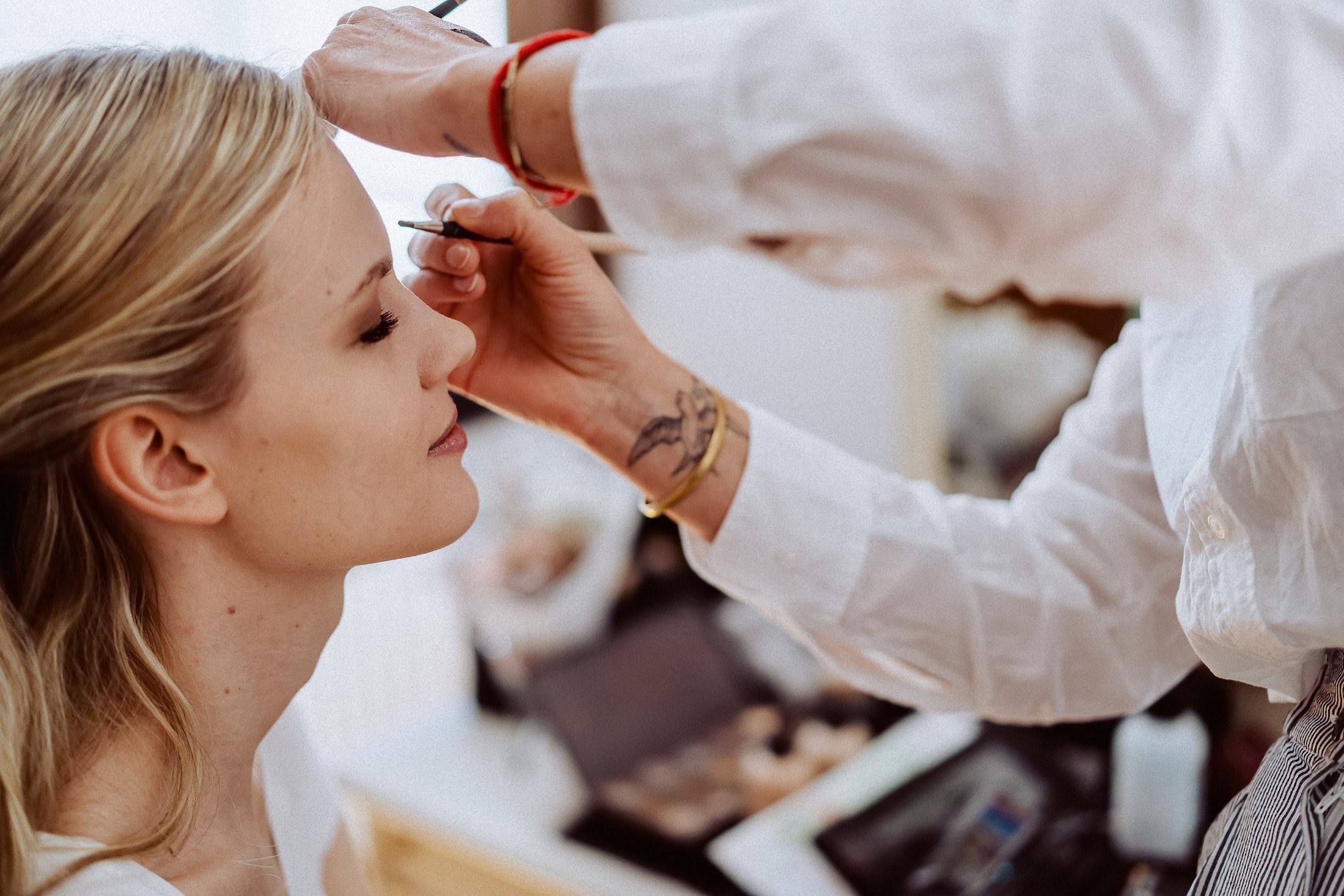 Der Braut wird der Lidstrich nachgezogen, am Handgelenk der Helferin ein Tattoo.