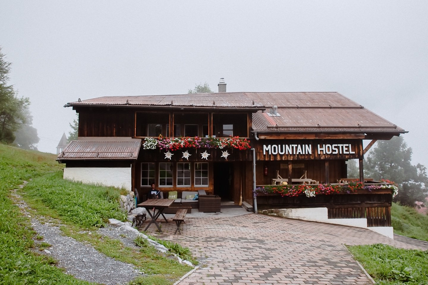 Holz-Berghostel mit roten Geranien und Schild, malerisch.
