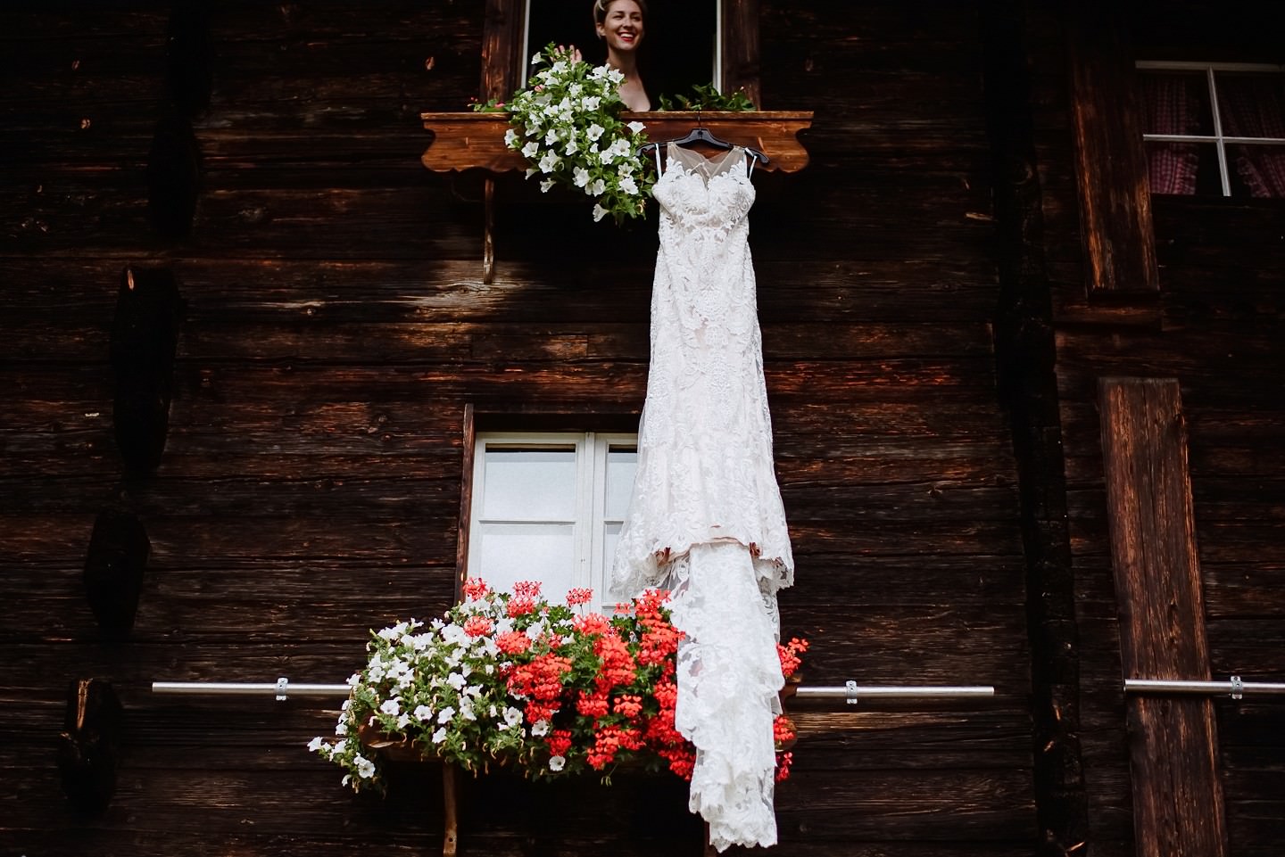 Hochzeitskleid hängend an Holzbalken, weiße Spitze, Geranien.