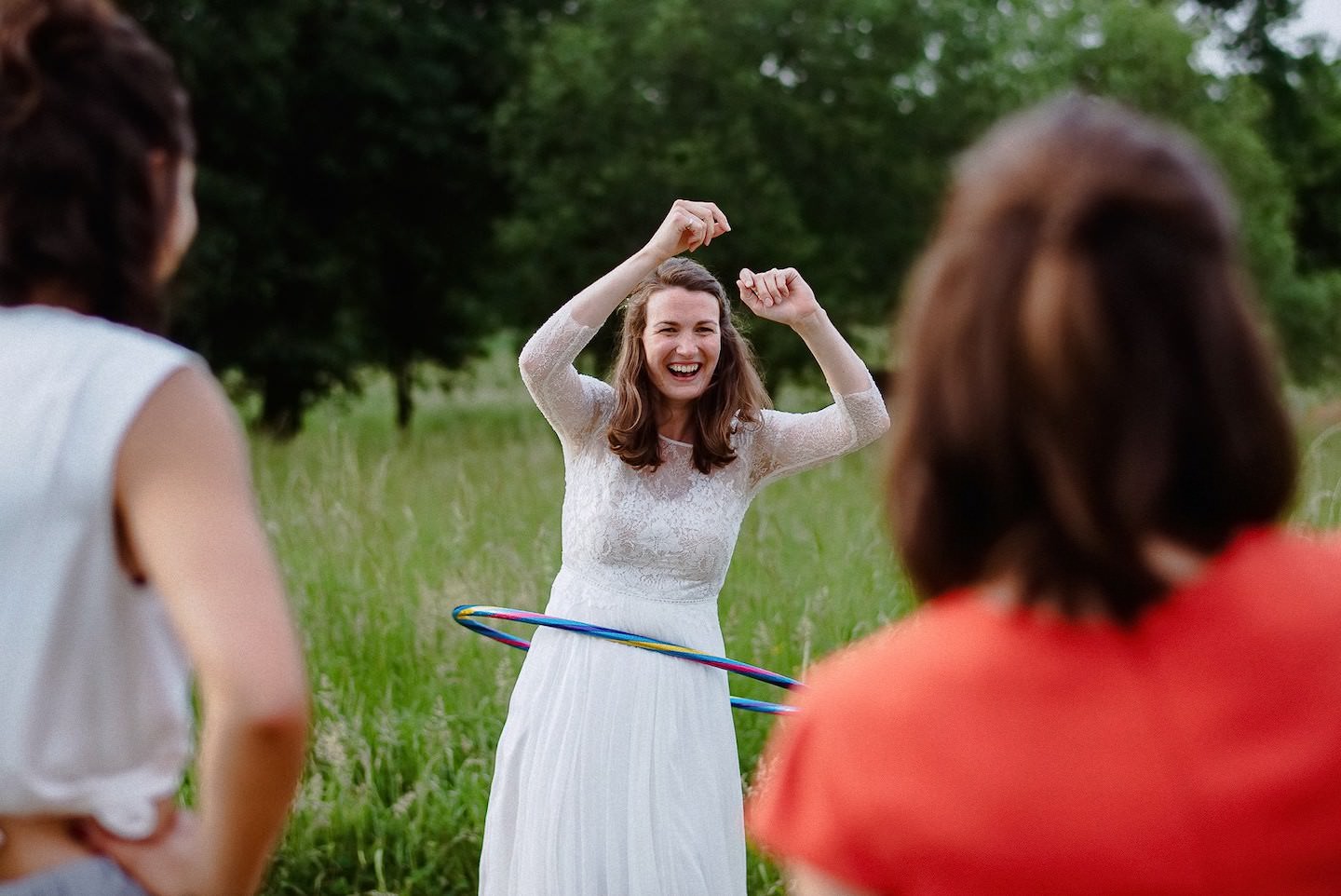 Braut tanzt Hula-Hoop auf Wiese, lachend, Gäste beobachten, Hochzeits-Game.
