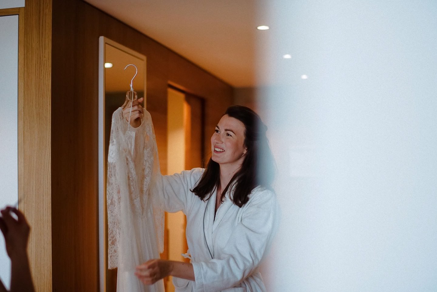 Braut zieht Kleid an, Hotelzimmer, warmes Licht, fröhliche Stimmung.