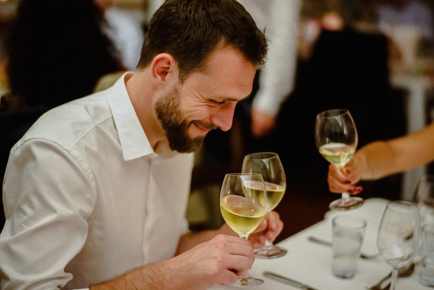 Gast trinkt lächelnd Weißwein beim Hochzeitsmahl, Portrait-Fokus, elegant.
