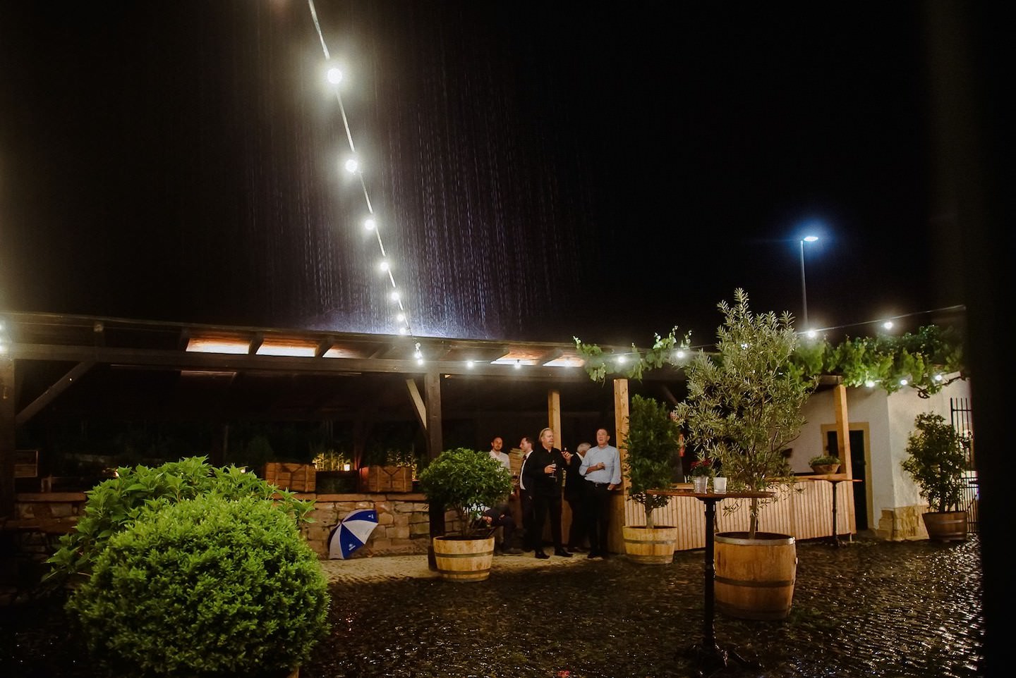 Hofgut Ruppertsberg Innenhof bei Nacht beleuchtet, Hochzeitsgäste feiern, Regen.