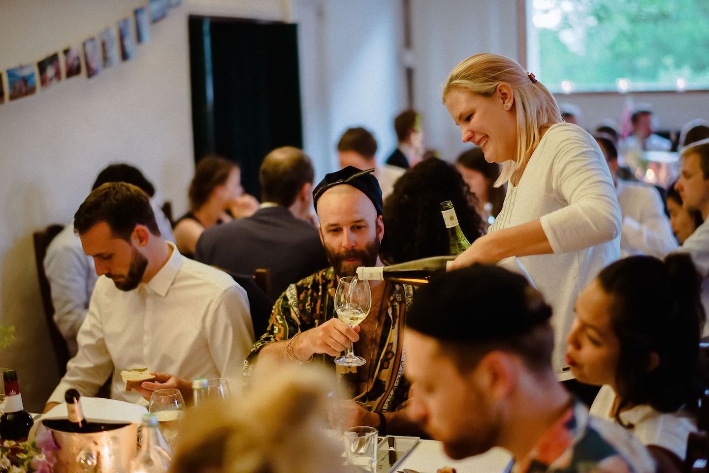 Kellnerin schenkt Weißwein beim Hochzeits-Dinner ein, Gäste beim Essen im Saal.