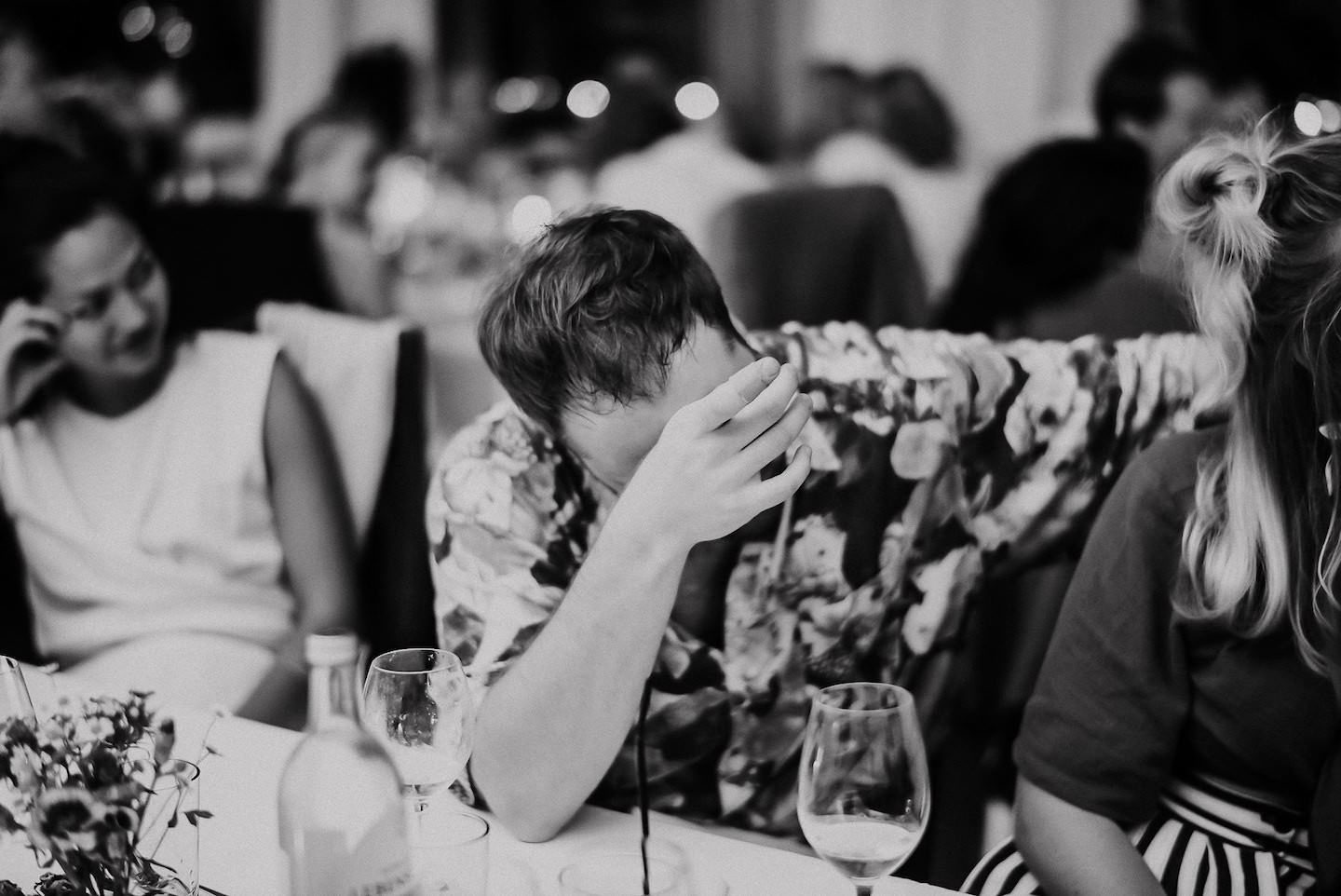 Kind isst konzentriert am Hochzeitstisch, Familie unscharf im Hintergrund, schwarz-weiß.