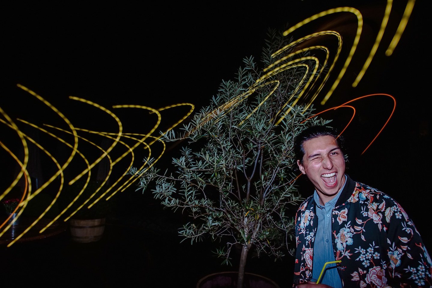 Hochzeitsgast lachend bei Light-Painting Effekt mit gelben Spiralen, Pflanze.