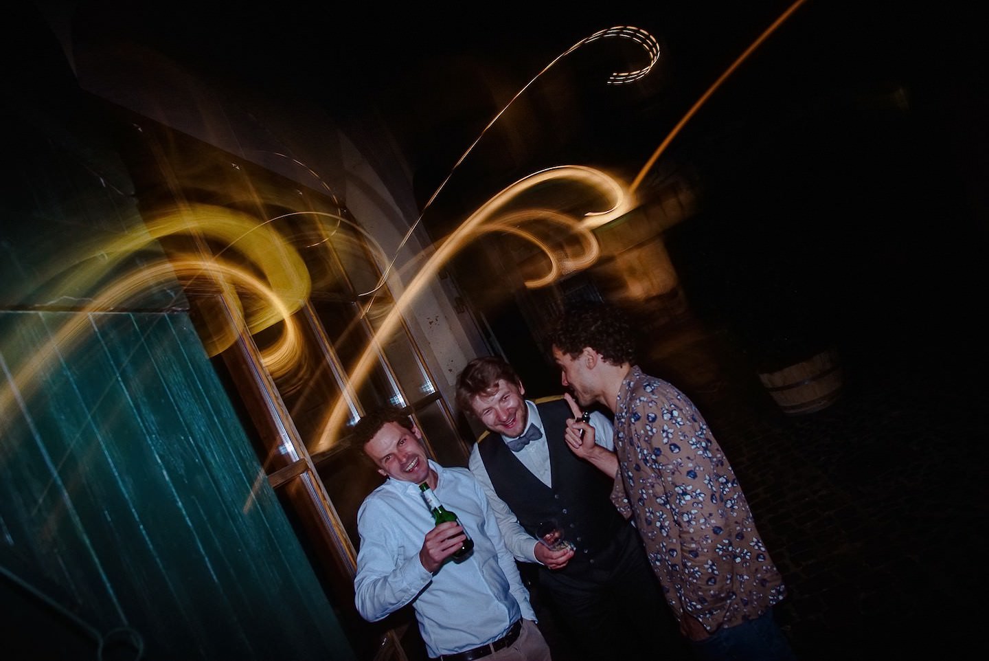Hochzeitsgäste-Trio beim Feiern mit goldenen Light-Painting-Spiralen hinter ihnen.