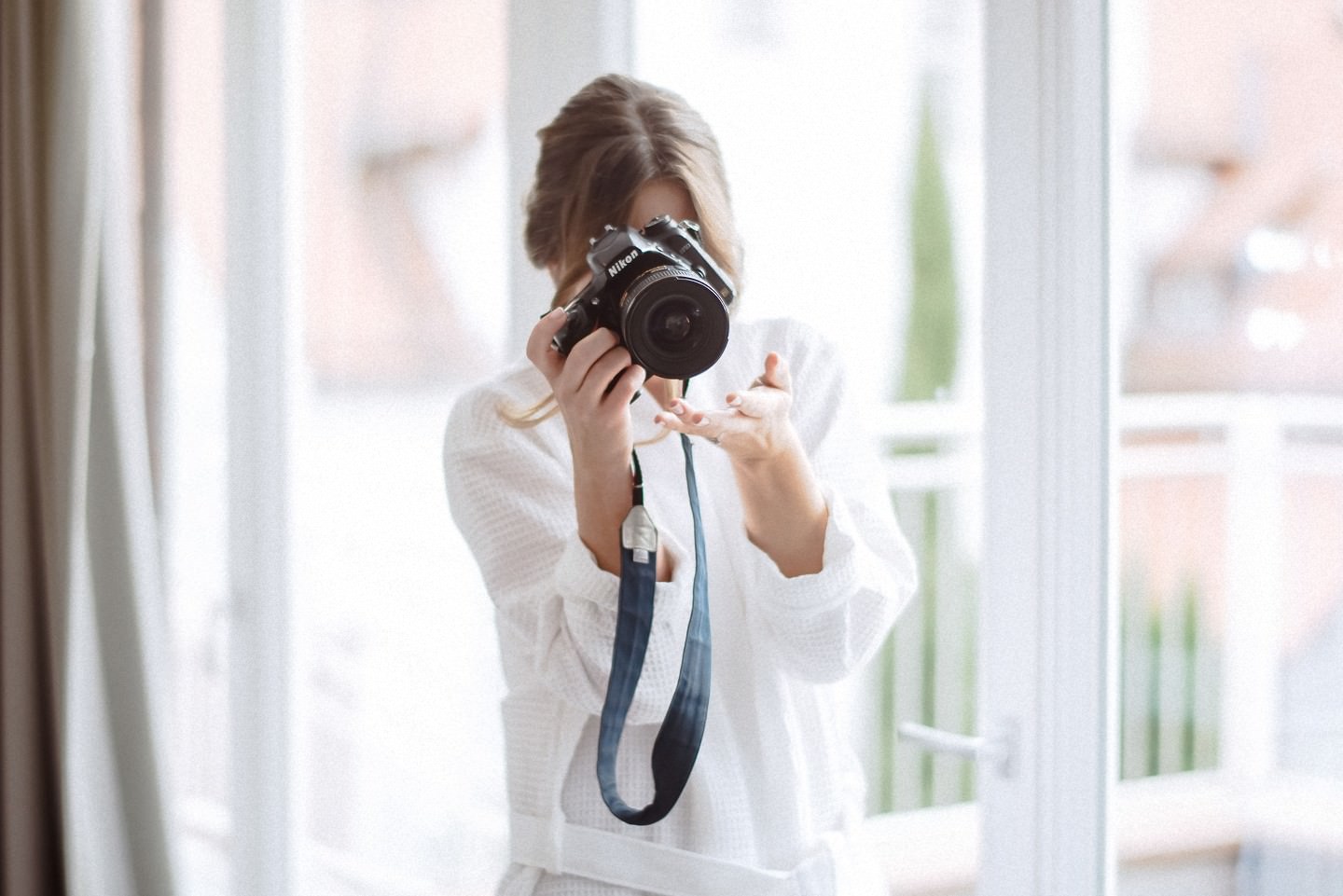 Braut fotografiert mit Nikon-Kamera, helles Hotelzimmer.