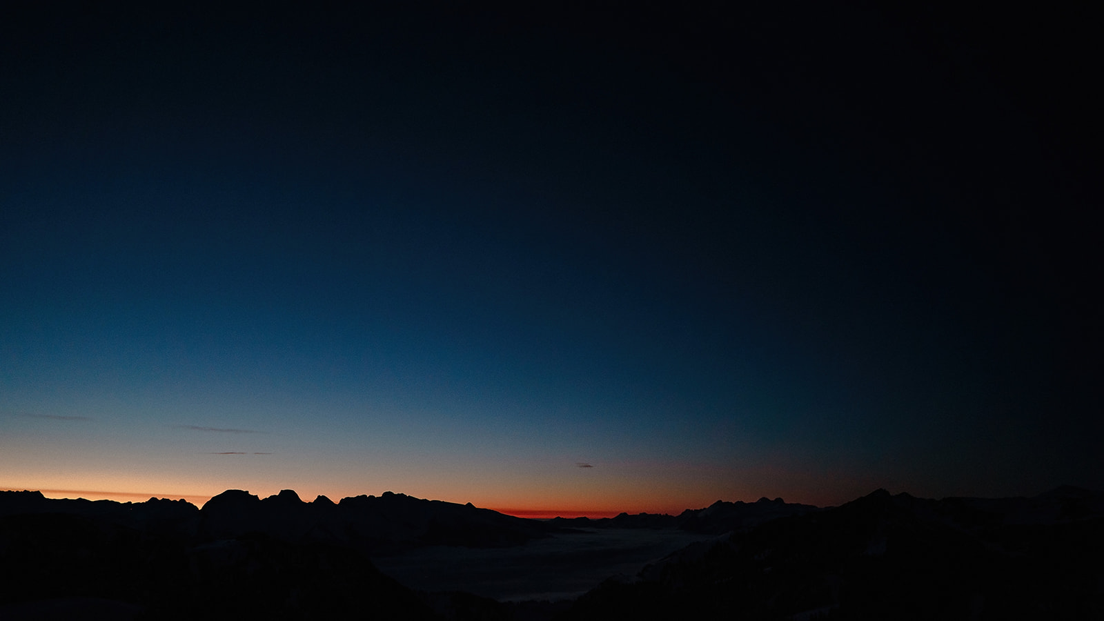 Orangefarbener Himmel über den Bergsilhouetten, Nebel liegt im Tal