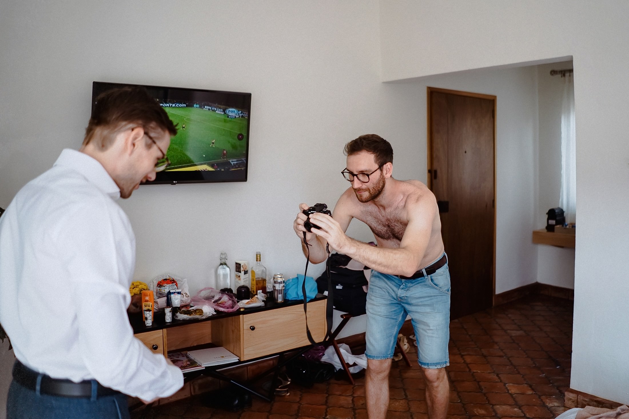 Der Bräutigam zeigt eine Kamera, während nebenan ein Fußballspiel auf dem Bildschirm läuft