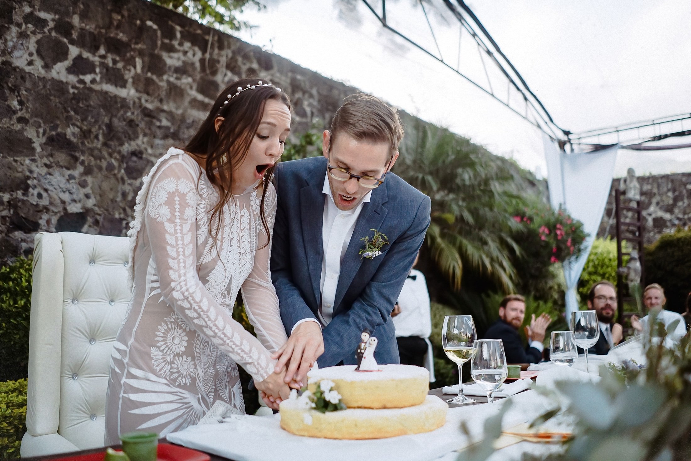 Das Brautpaar schneidet gemeinsam die Hochzeitstorte unter einem Steingewölbe, die Gäste schauen zu