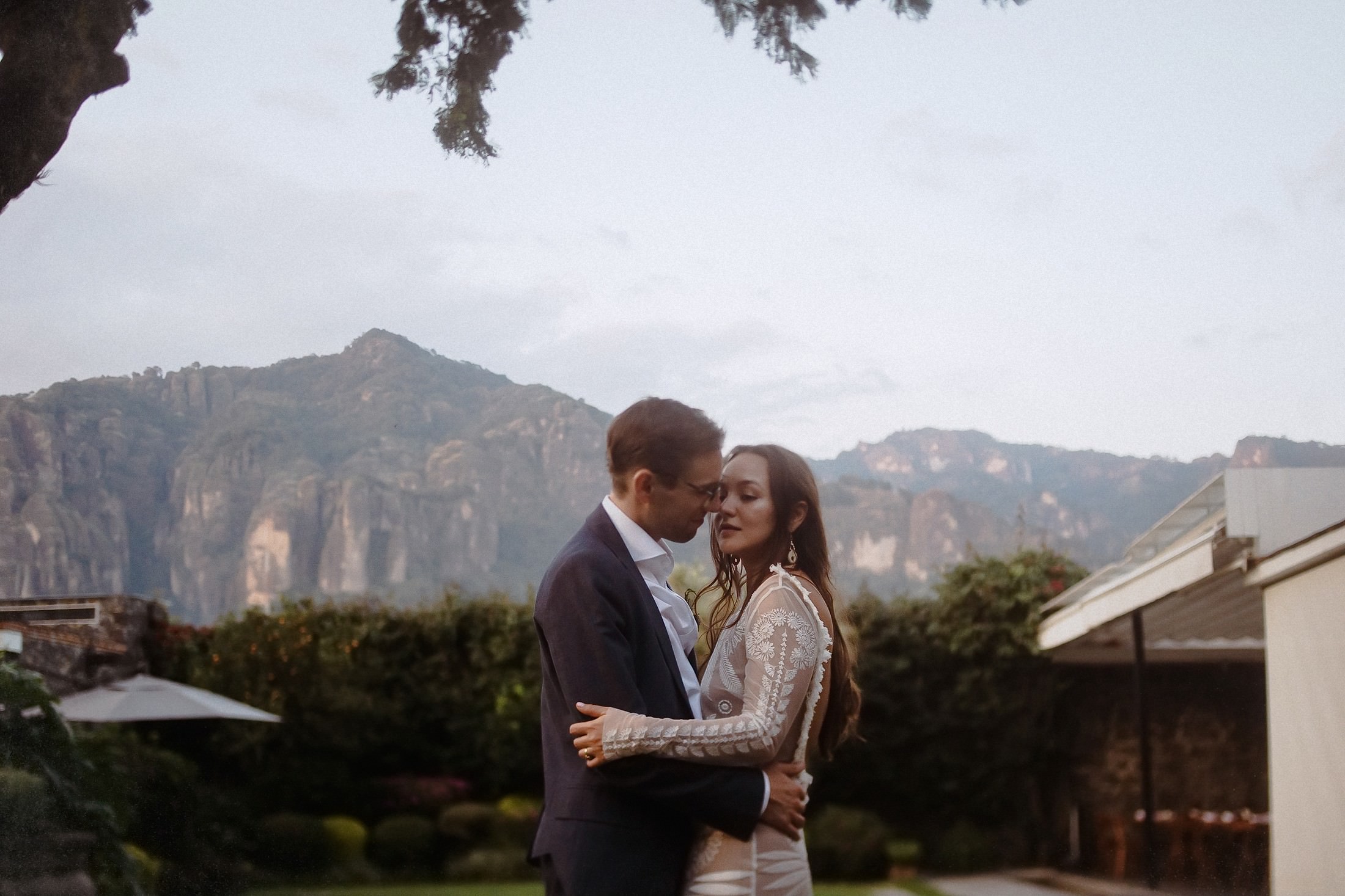 Das Brautpaar umarmt sich vor dem bergigen Panorama von Tepoztlán im zarten Morgenlicht
