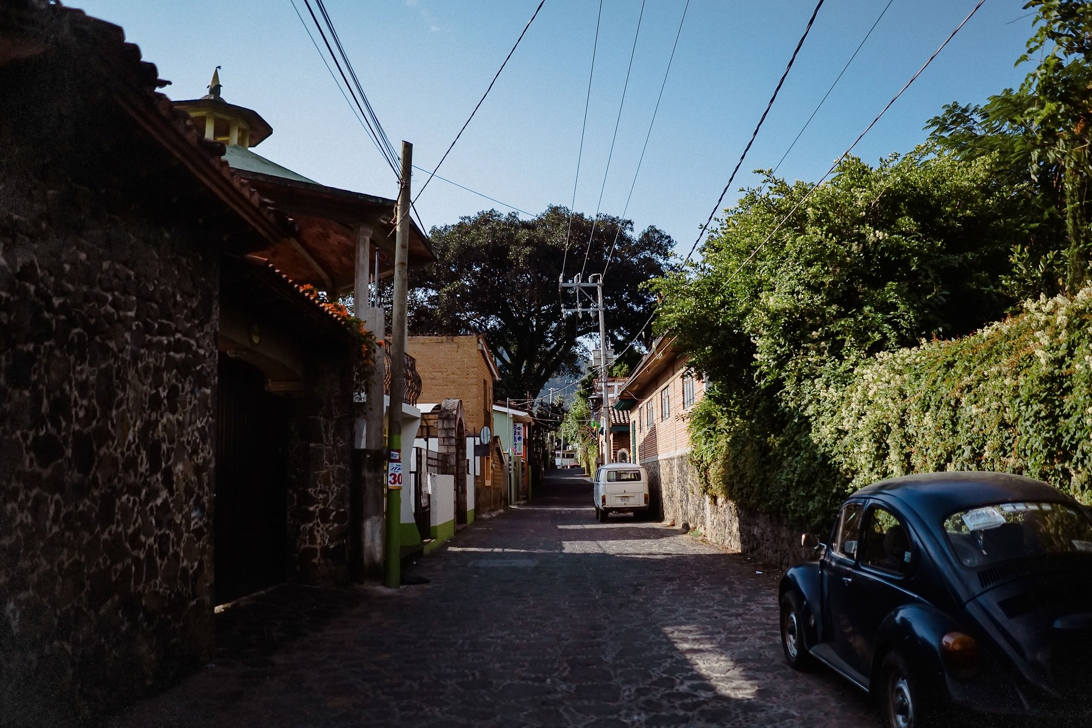Eine enge Kopfsteinpflaster-Gasse in Tepoztlán zeigt einen alten blauen VW-Käfer vor Steinmauern
