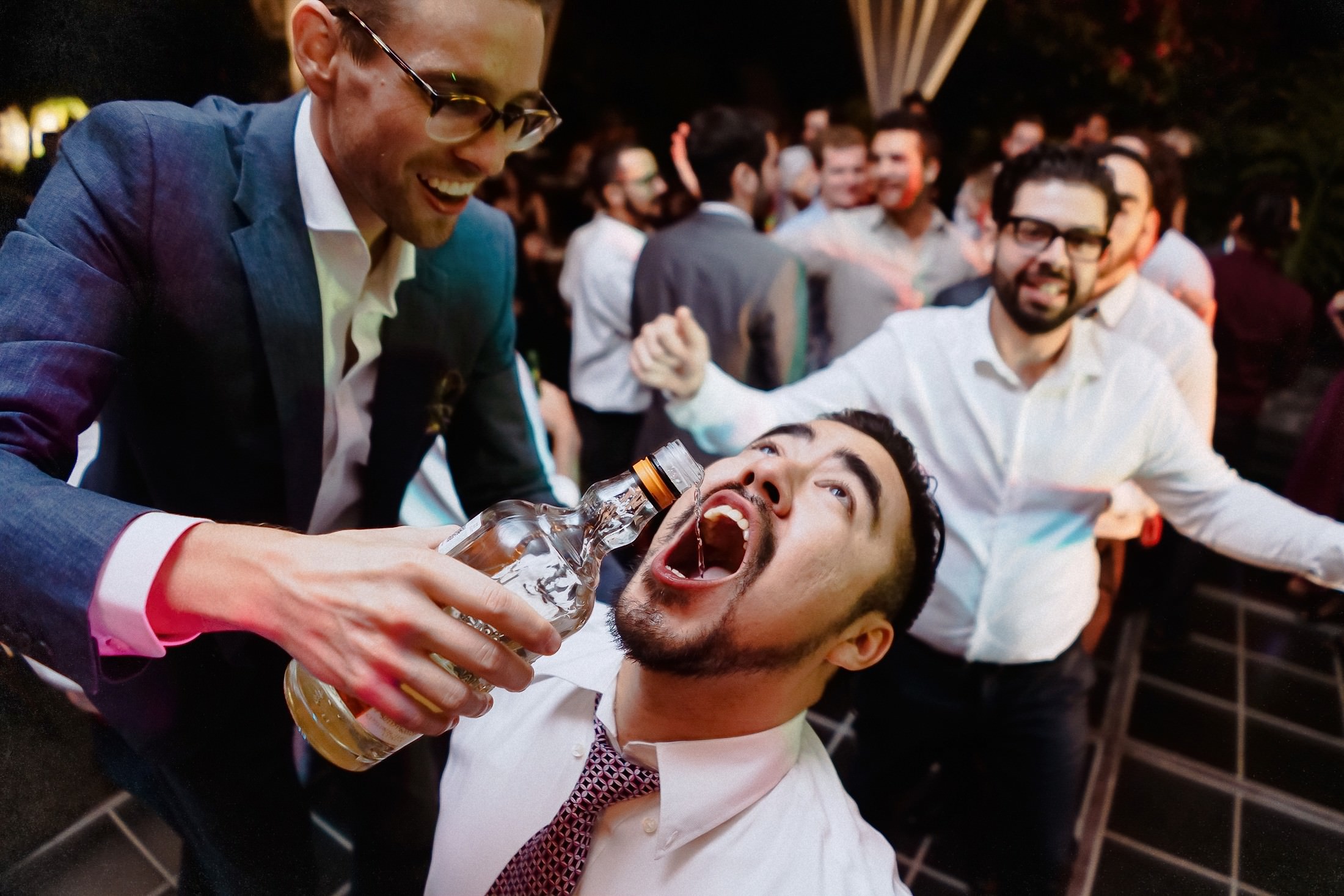 Ein Gast trinkt Mezcal mit zurückgeworfenem Kopf, während der Bräutigam lachend die Flasche hält