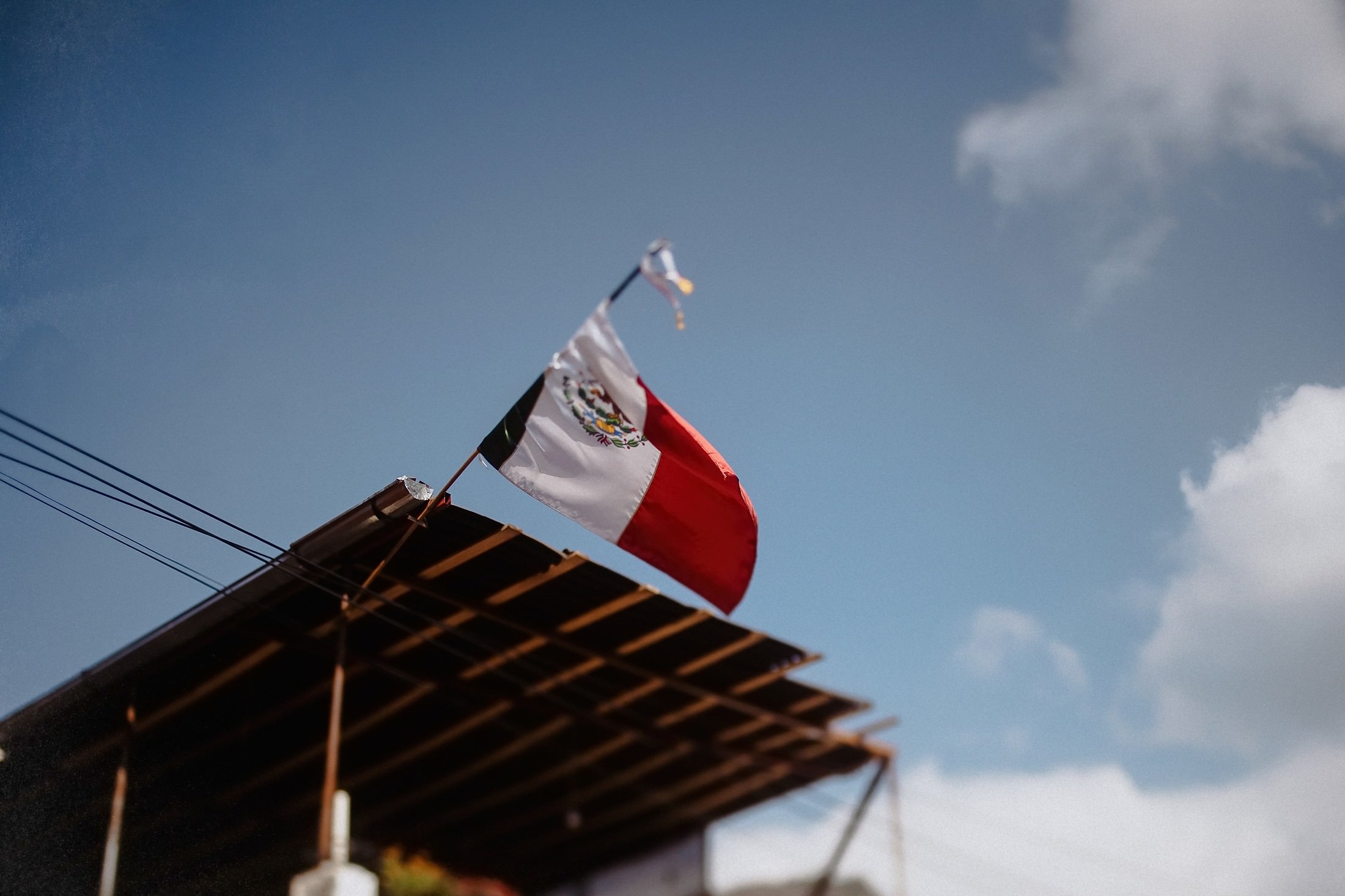 Die mexikanische Flagge weht am blauen Himmel vor einem Metallvordach