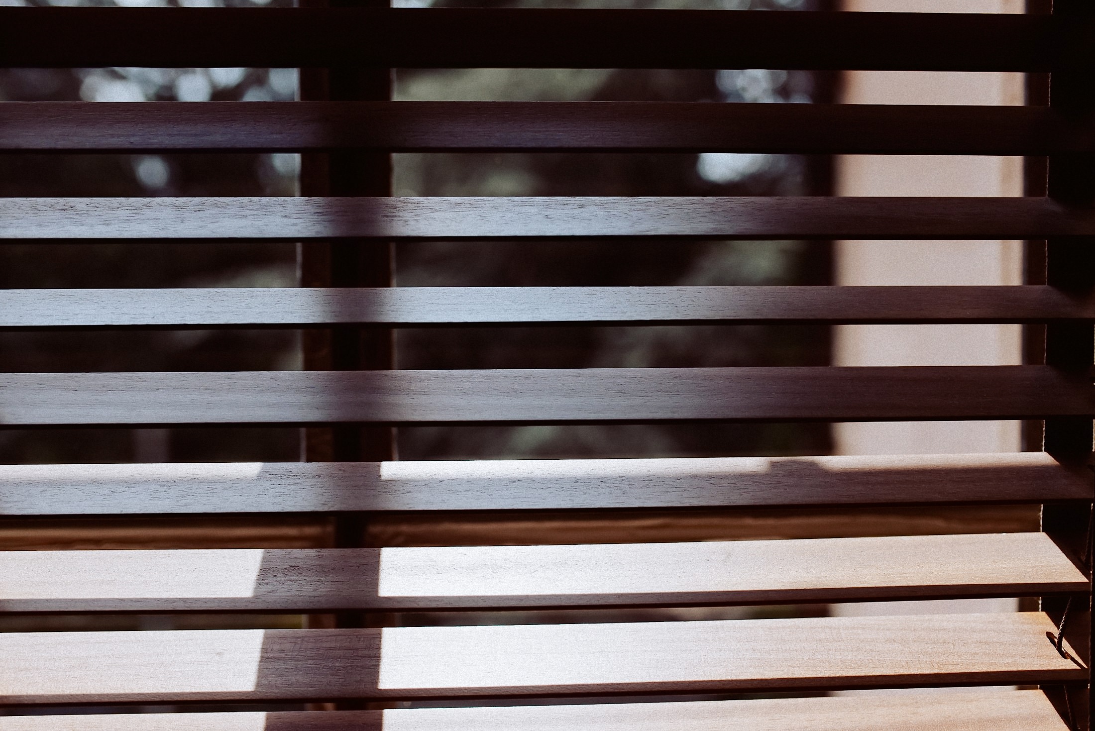 Holzjalousien mit Licht-Schatten-Spiel durchs Hotelzimmerfenster.