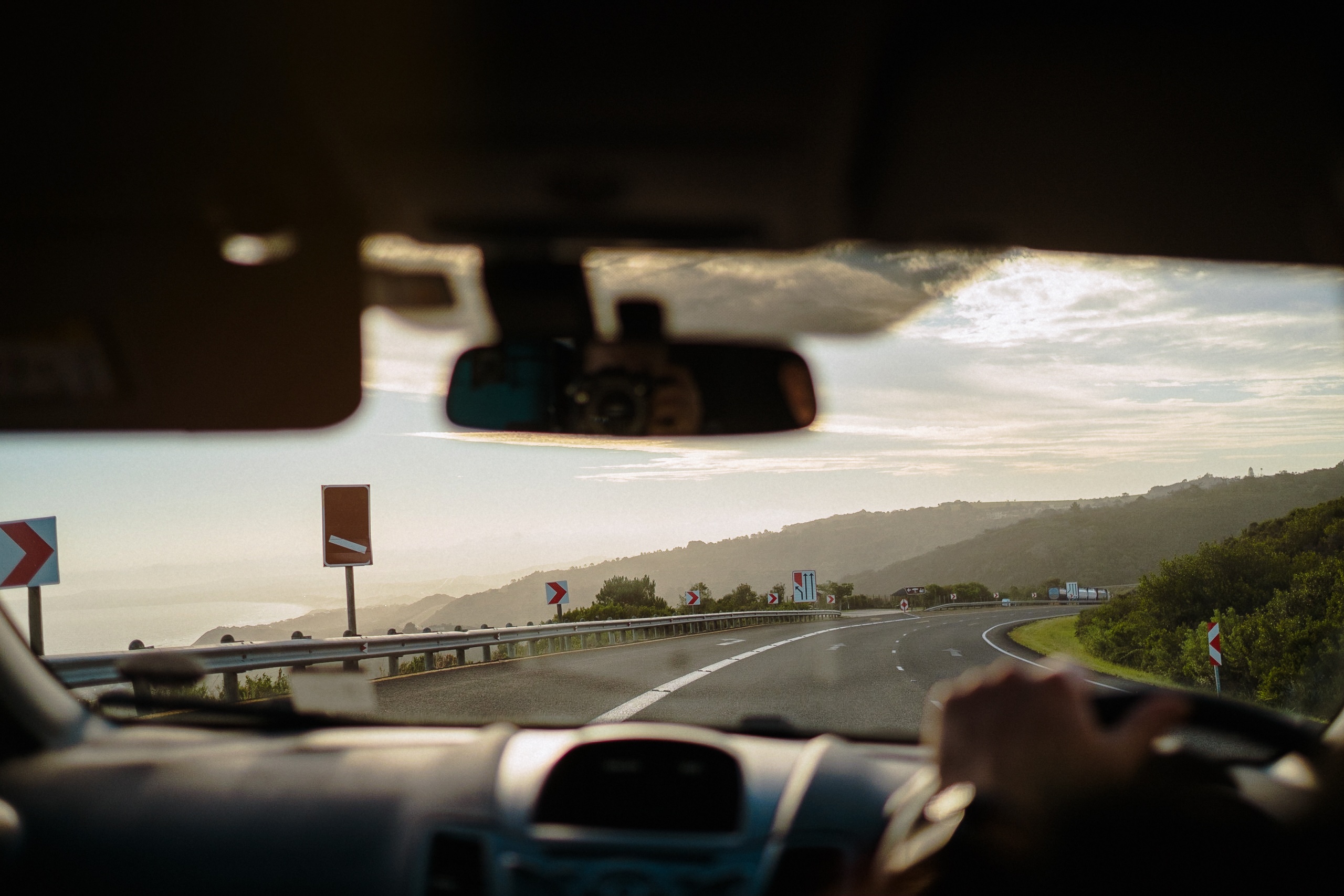 Fahrt über die Küstenstraße am Meer entlang, Hand am Lenkrad im Gegenlicht