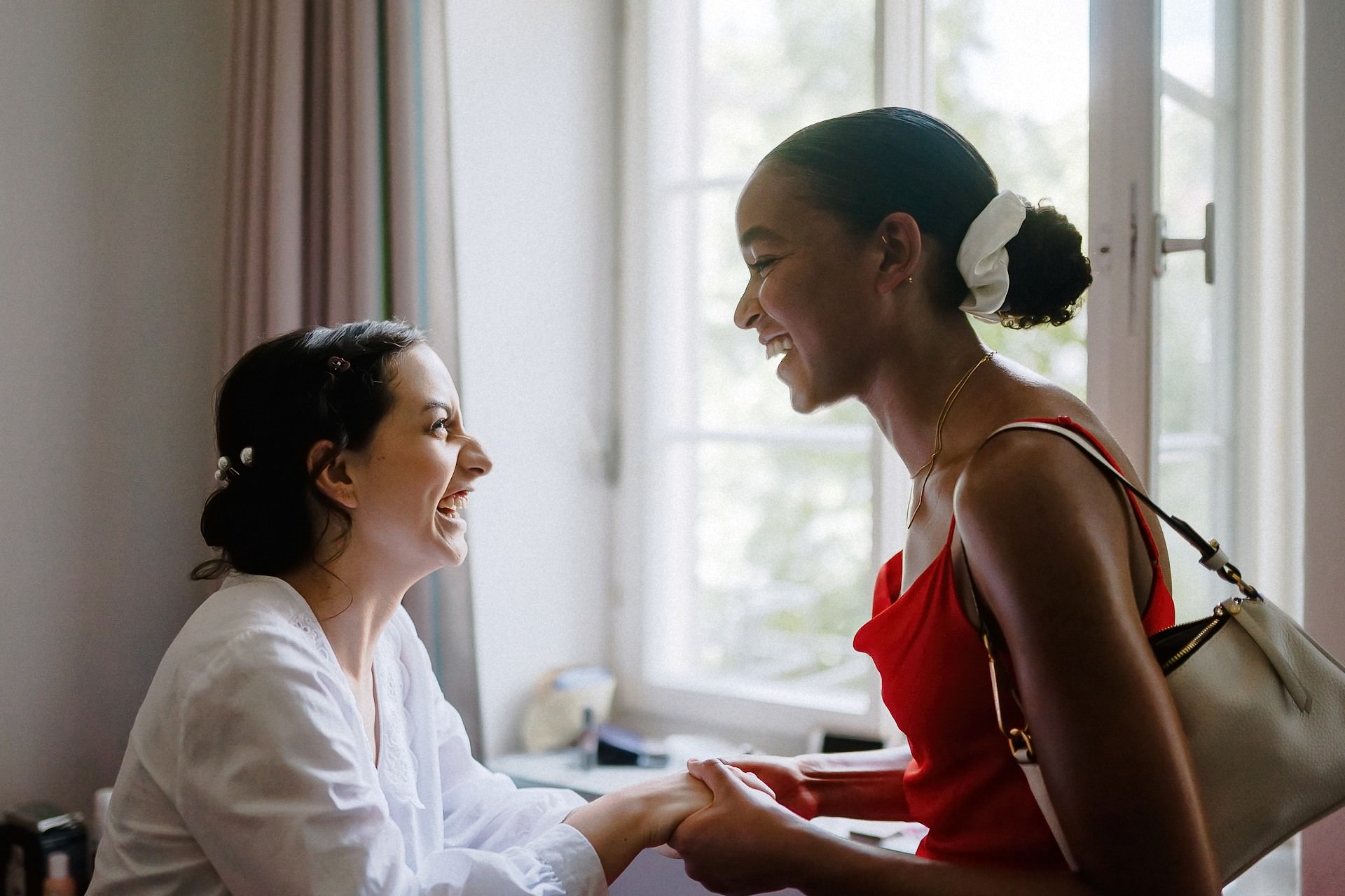 Braut und Freundin umarmen sich freudig im Hotelzimmer, intensive Emotion.