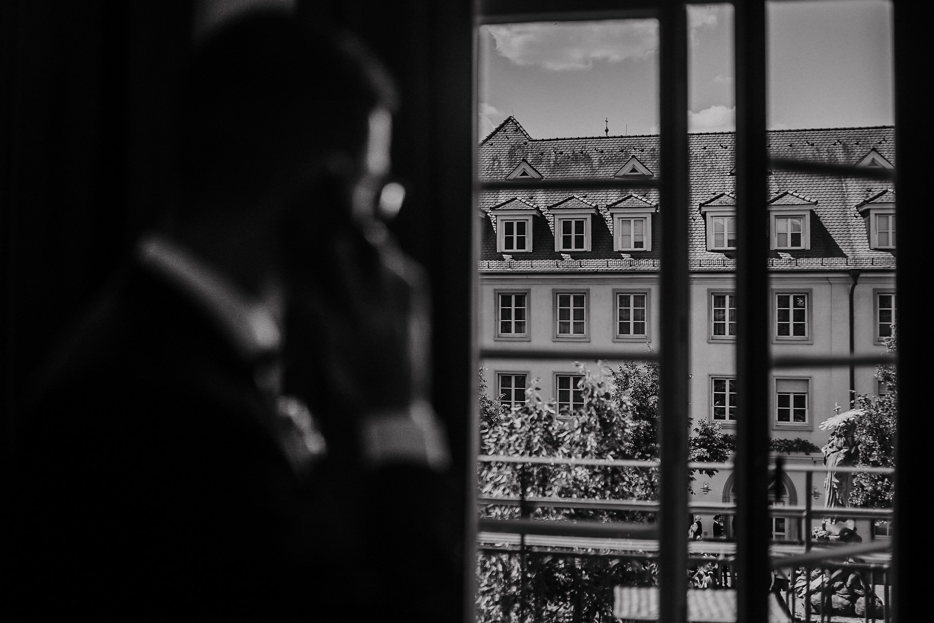 Silhouette des Bräutigams am Fenster, Blick auf die Altbaufassade gegenüber.