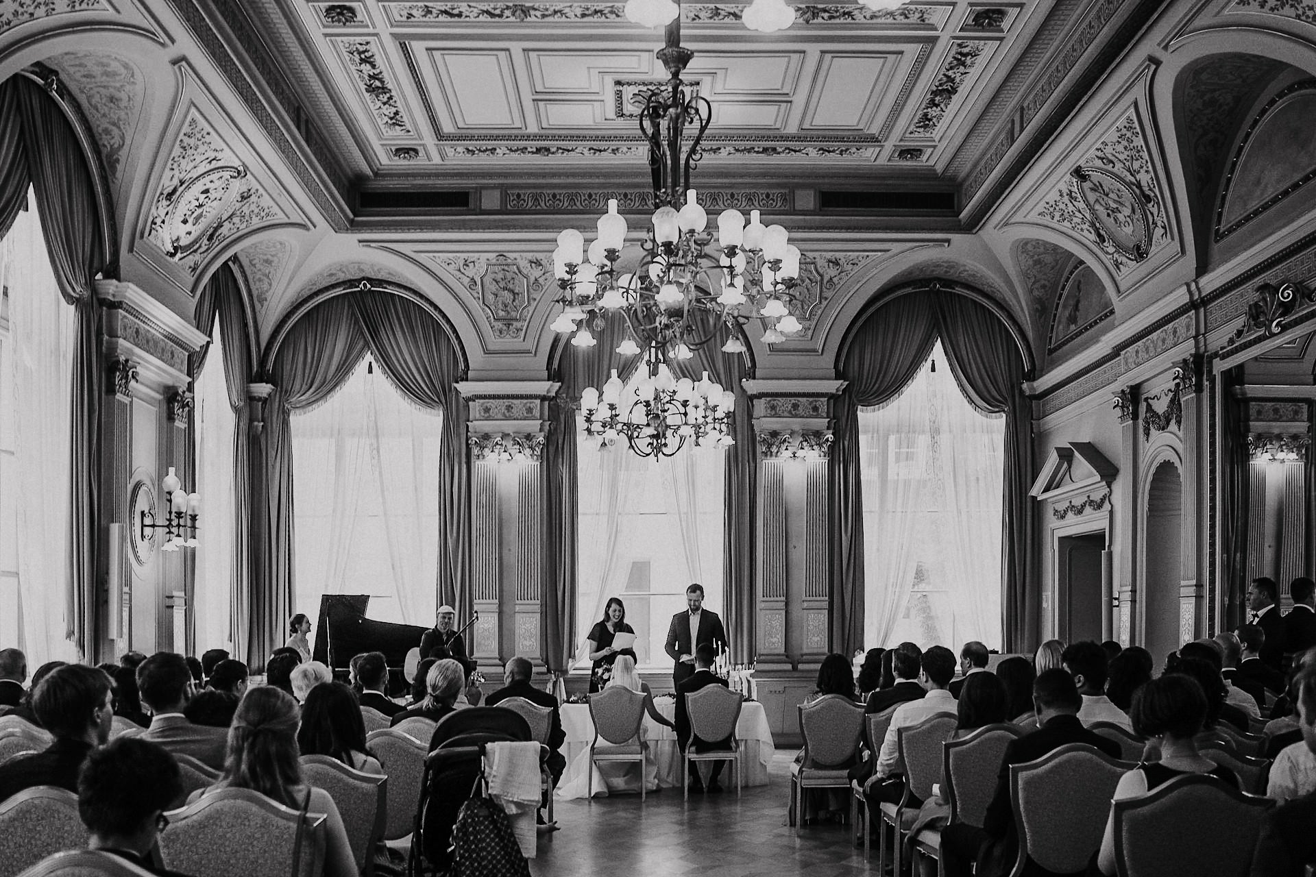 Standesbeamte und Gäste im eleganten Trausaal mit Kronleuchter während der Zeremonie.