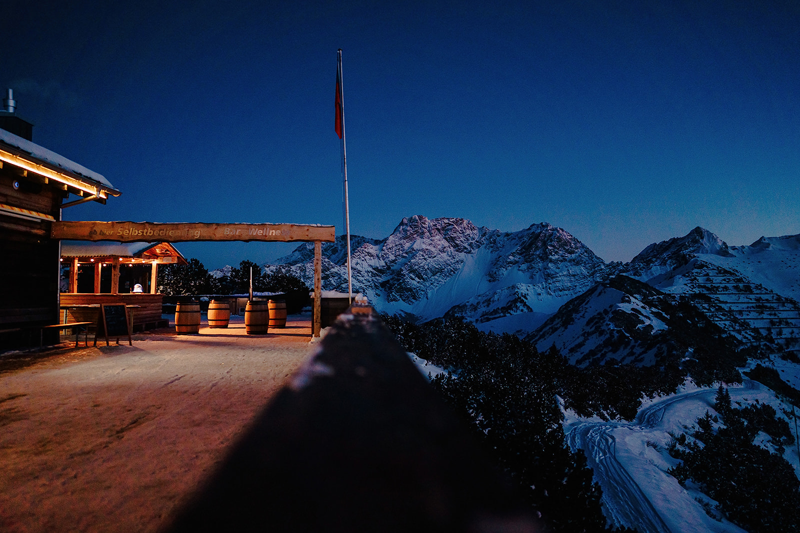 Die Berghütte mit Lichterkette und Fahnenmast im letzten Dämmerlicht