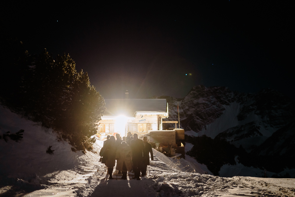 Silhouetten der Gäste auf dem Schneeweg zur hell erleuchteten Berghütte