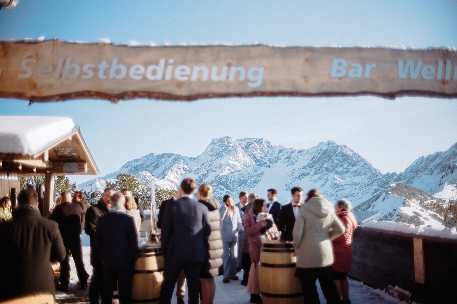Die Gäste stehen an Holzfässern vor der Selbstbedienungsbar der Berghütte