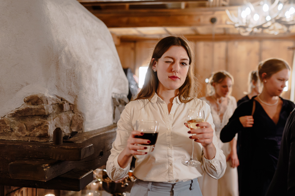 Eine Gästin zwinkert mit einem Glas Rot- und einem Glas Weißwein in die Kamera