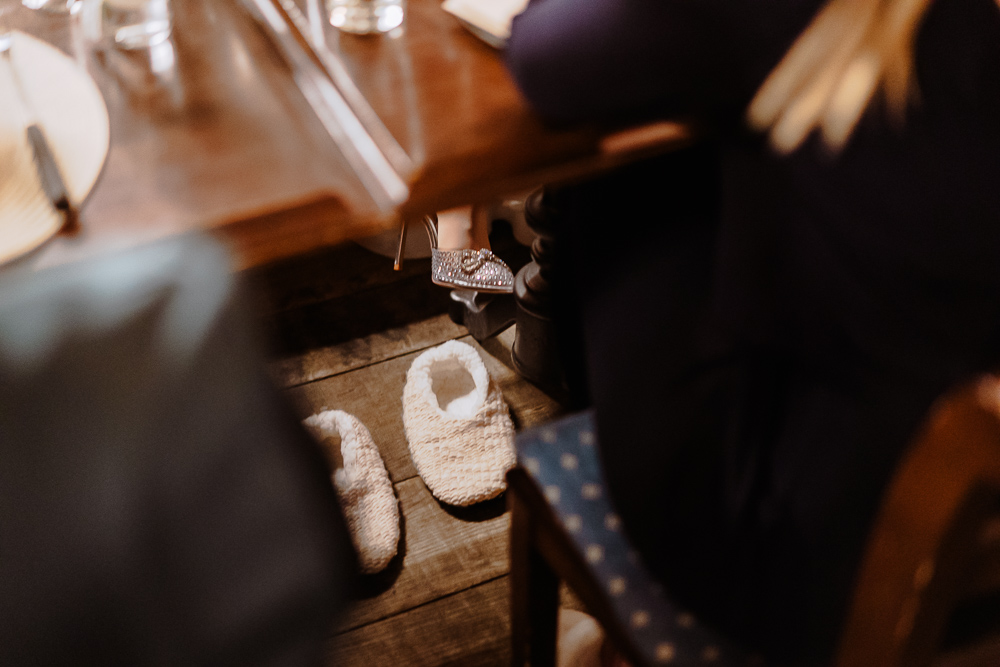 Unter dem Tisch stehen gestrickte Hüttenschuhe neben einem silbernen Absatzschuh