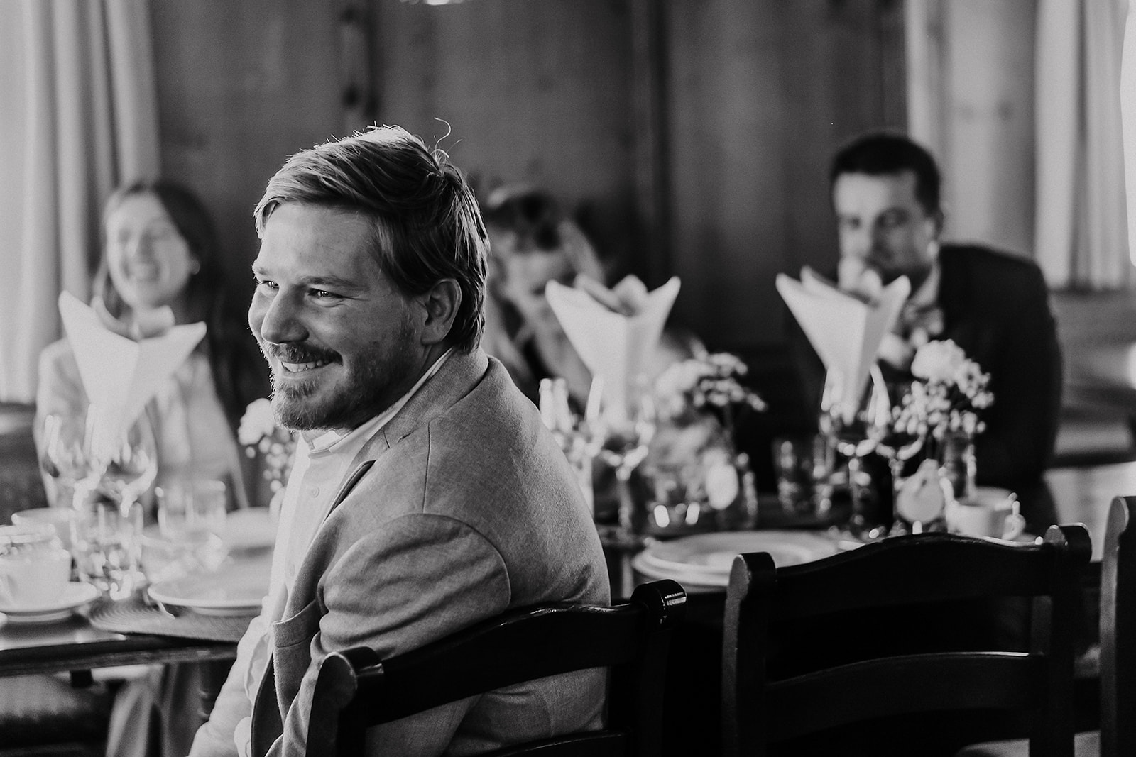 Ein Gast lacht an der Tafel, dahinter unscharf die festlich gedeckten Tische