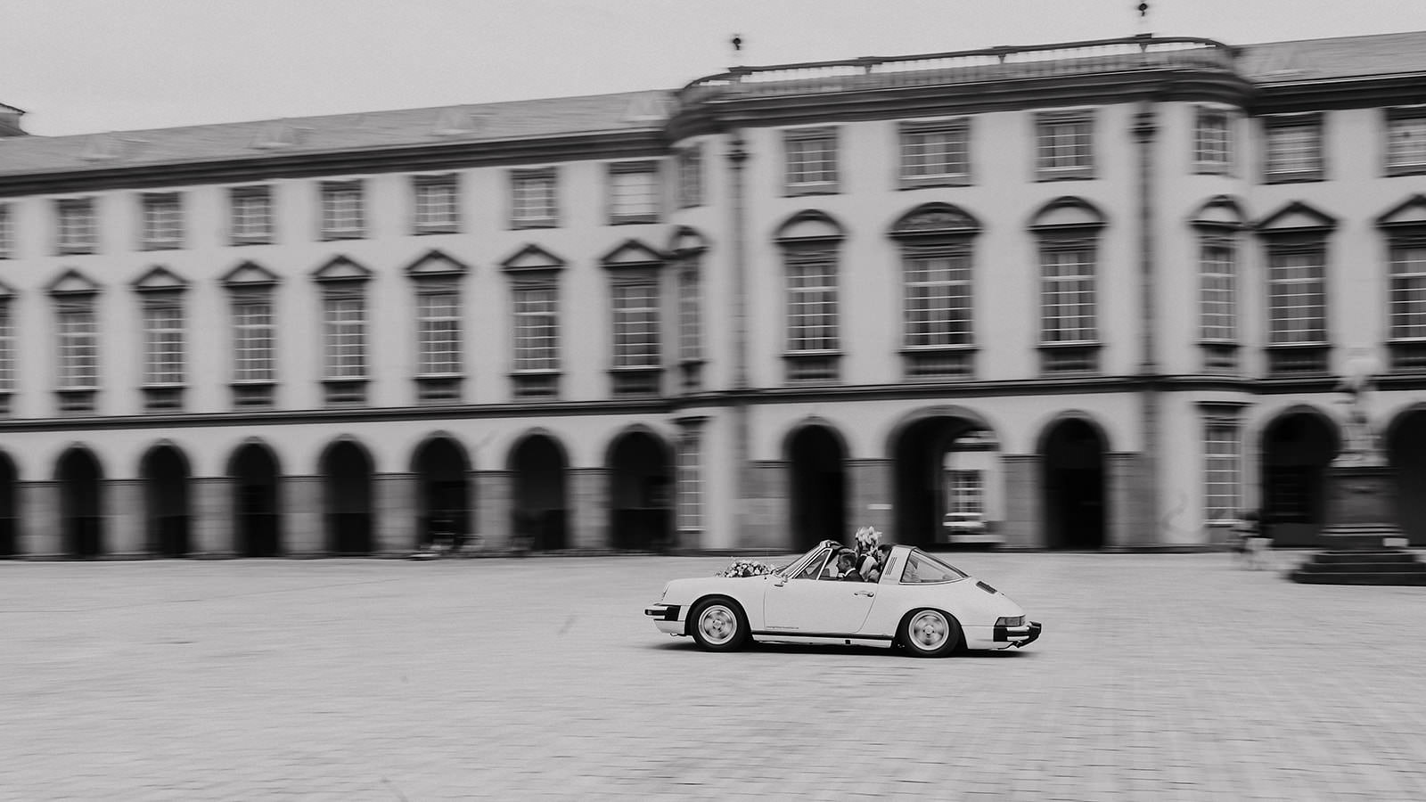 Ein weißer Porsche 911 wartet vor der Fassade des Schlosses