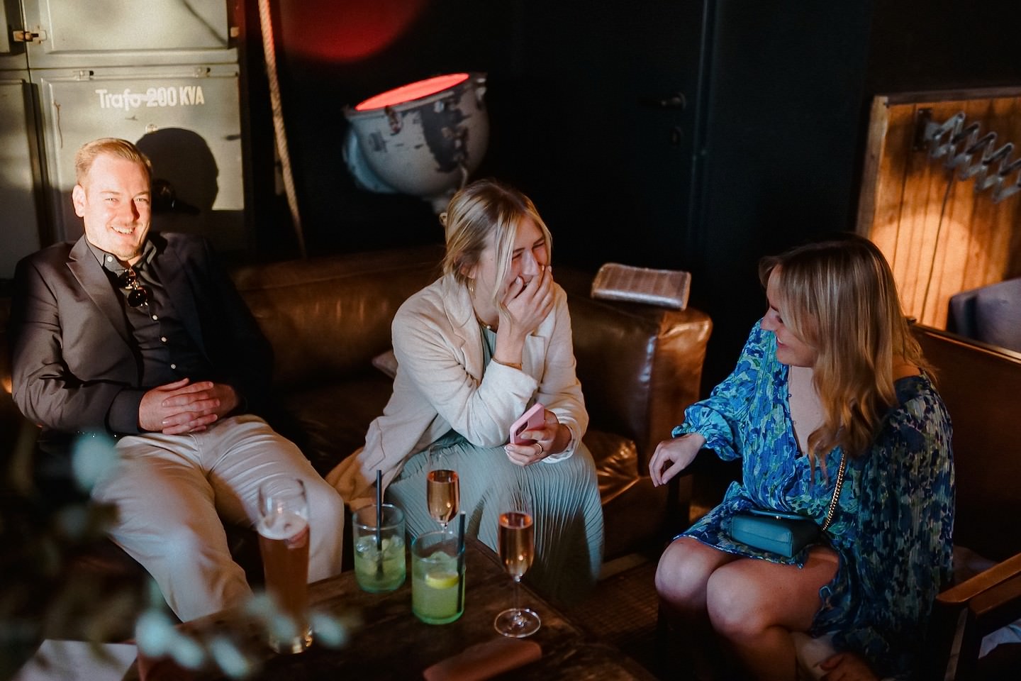 Drei Gäste lachen zusammen auf dem Ledersofa der Lounge