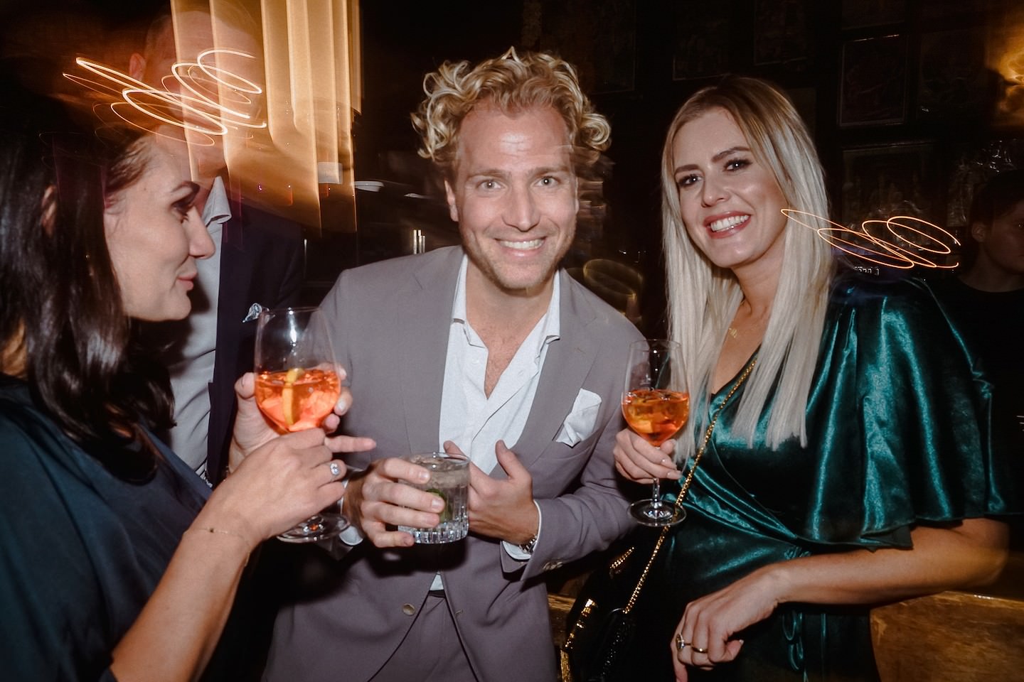 Drei Gäste posieren lachend mit Drinks bei der Abendparty