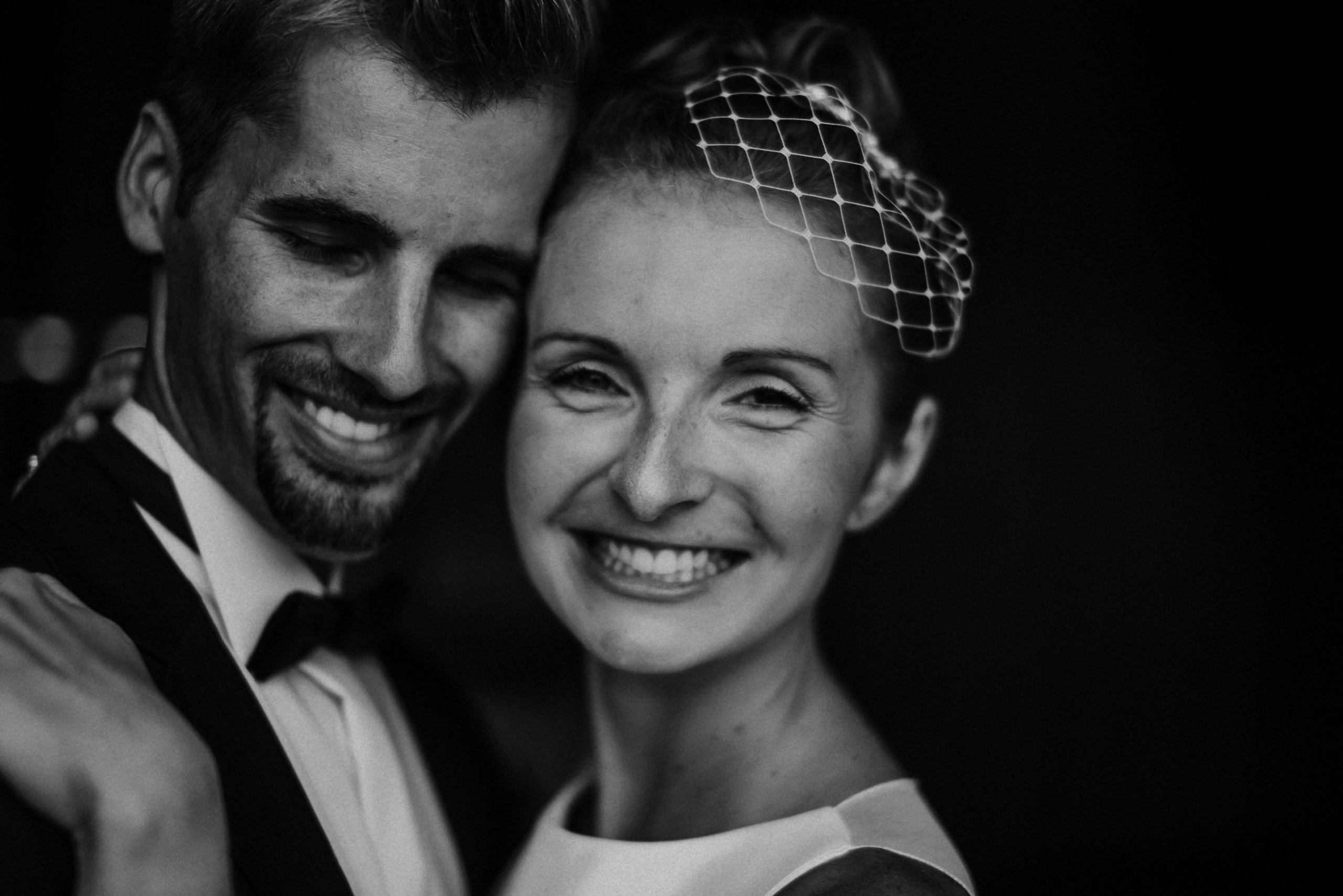 Nahes Paarportrait: Braut mit Birdcage-Schleier und Bräutigam lachen, schwarzweiß.