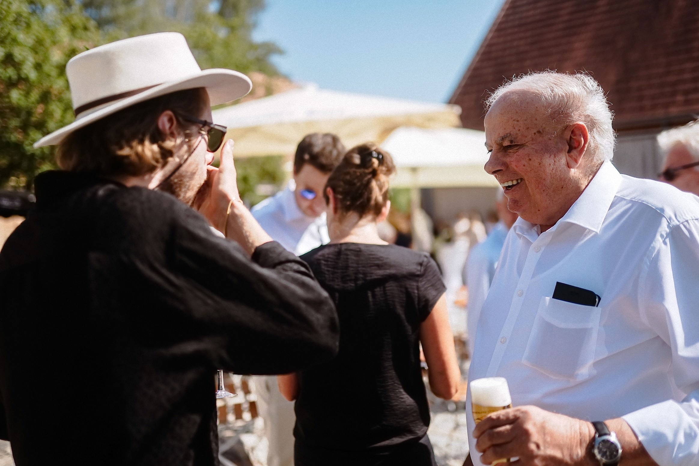 Bräutigam lacht mit einem älteren Herrn, der ein Bier in der Hand hält.